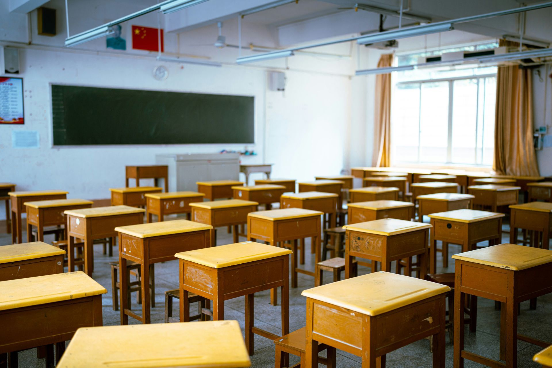 Empty classroom with rows of desks, windows, and natural light streaming in.