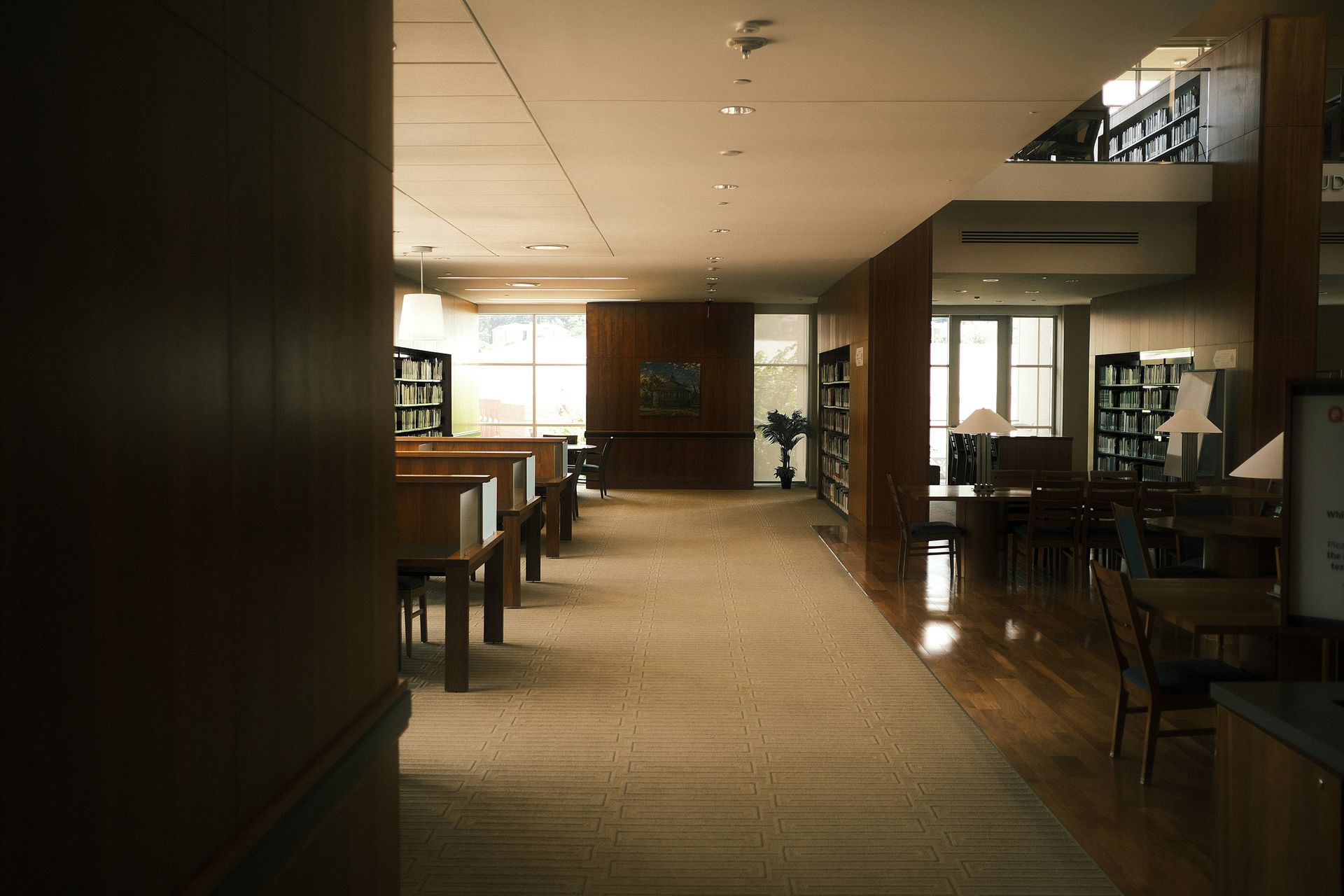 Empty ballroom with large windows, dark carpet, and hanging chandelier.