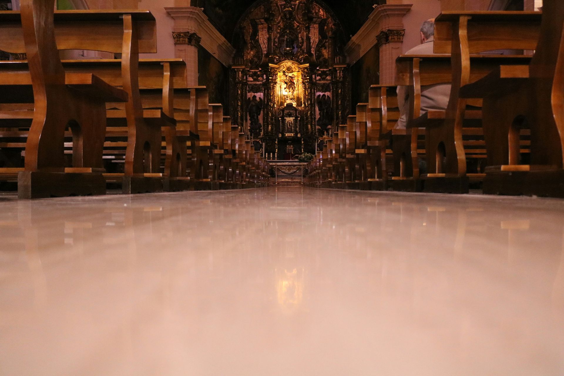 Interior of a church with rows of wooden pews facing an open doorway to a grassy area. Bright natural light.