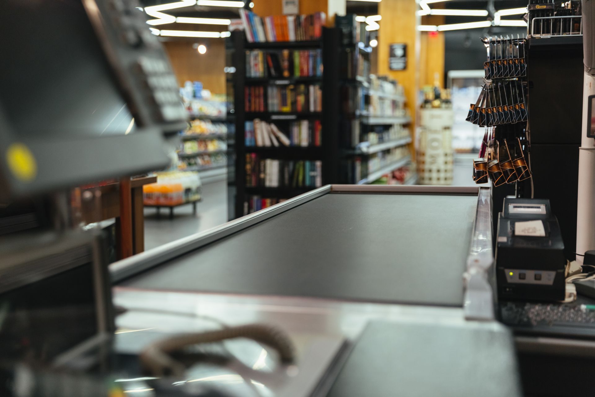 Cash register at a store checkout counter; shelves of books and groceries in the background.