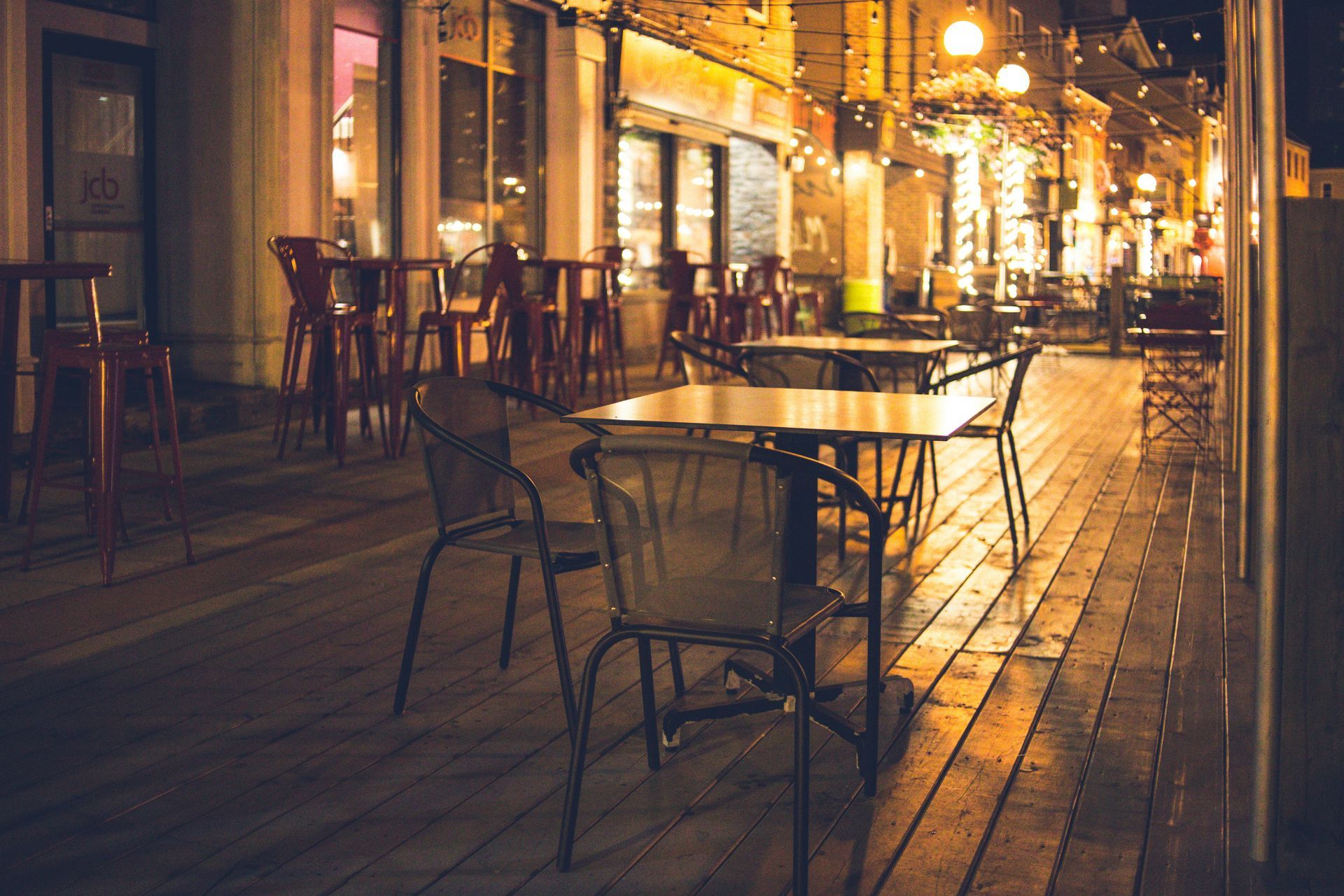 Outdoor restaurant patio at night with tables, chairs, and streetlights.