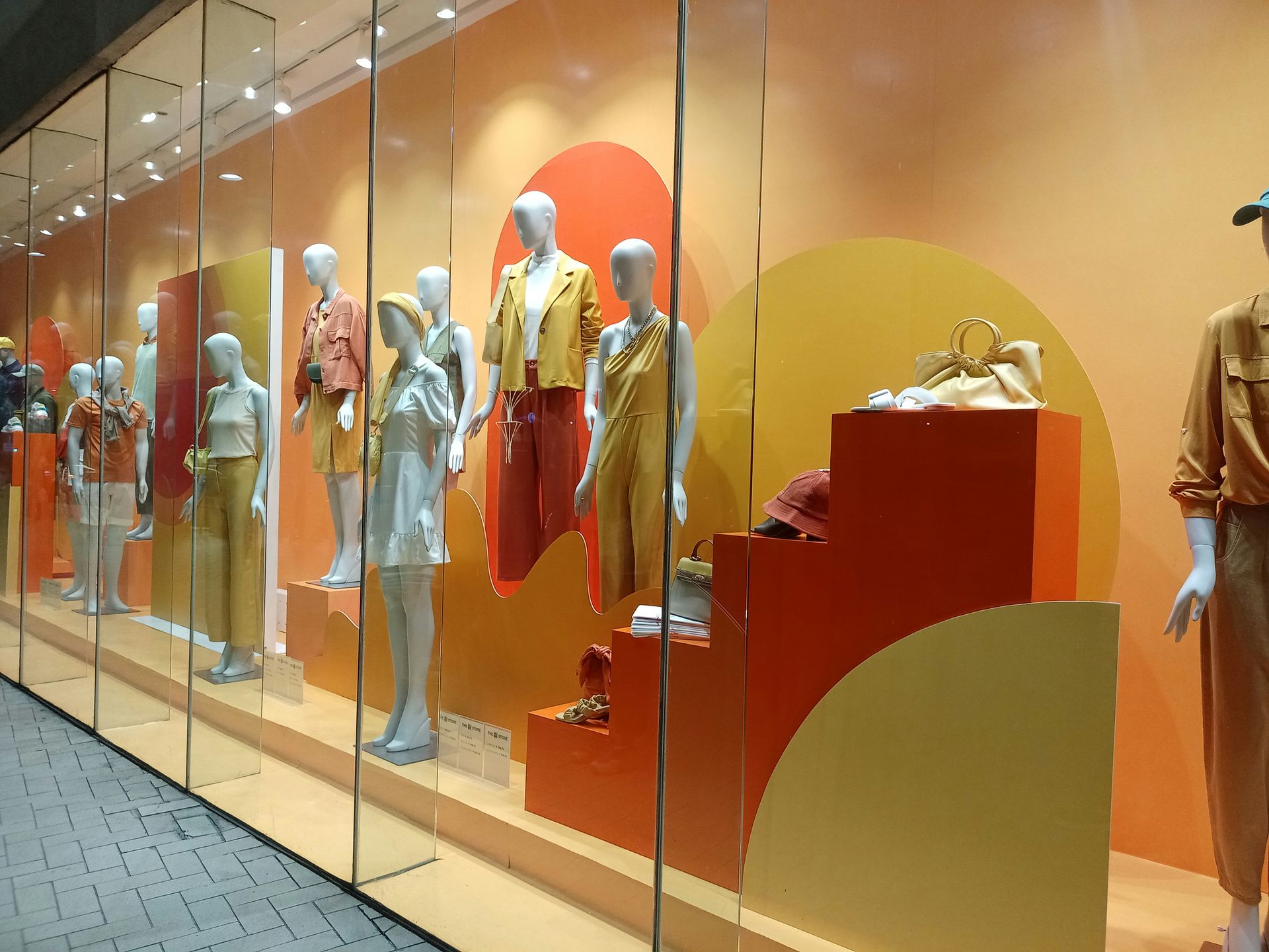 Store window display with mannequins in orange and yellow clothing; setting is orange-toned.