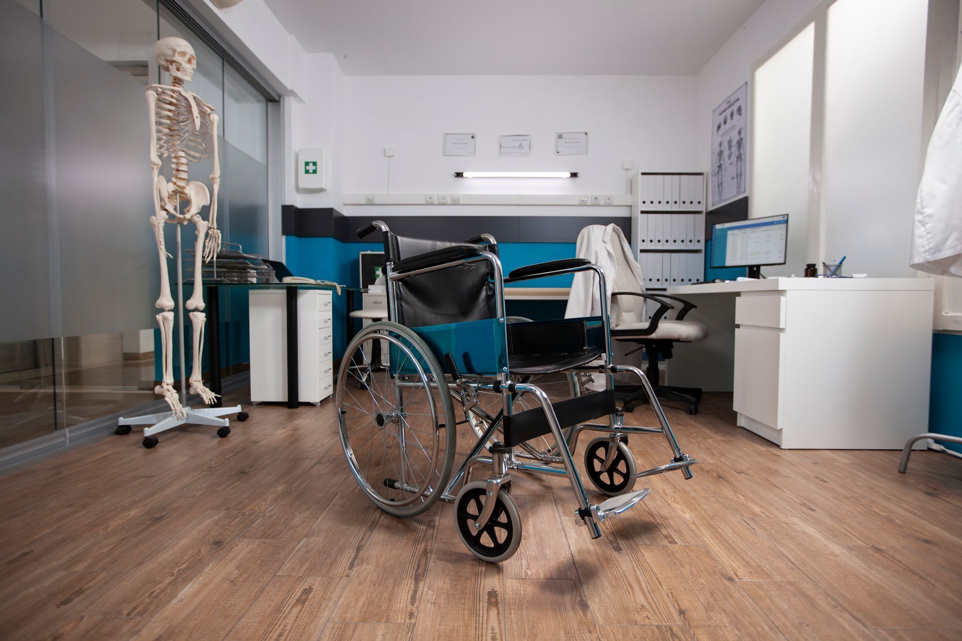 Wheelchair in a doctor's office with a skeleton, desk, and medical charts.