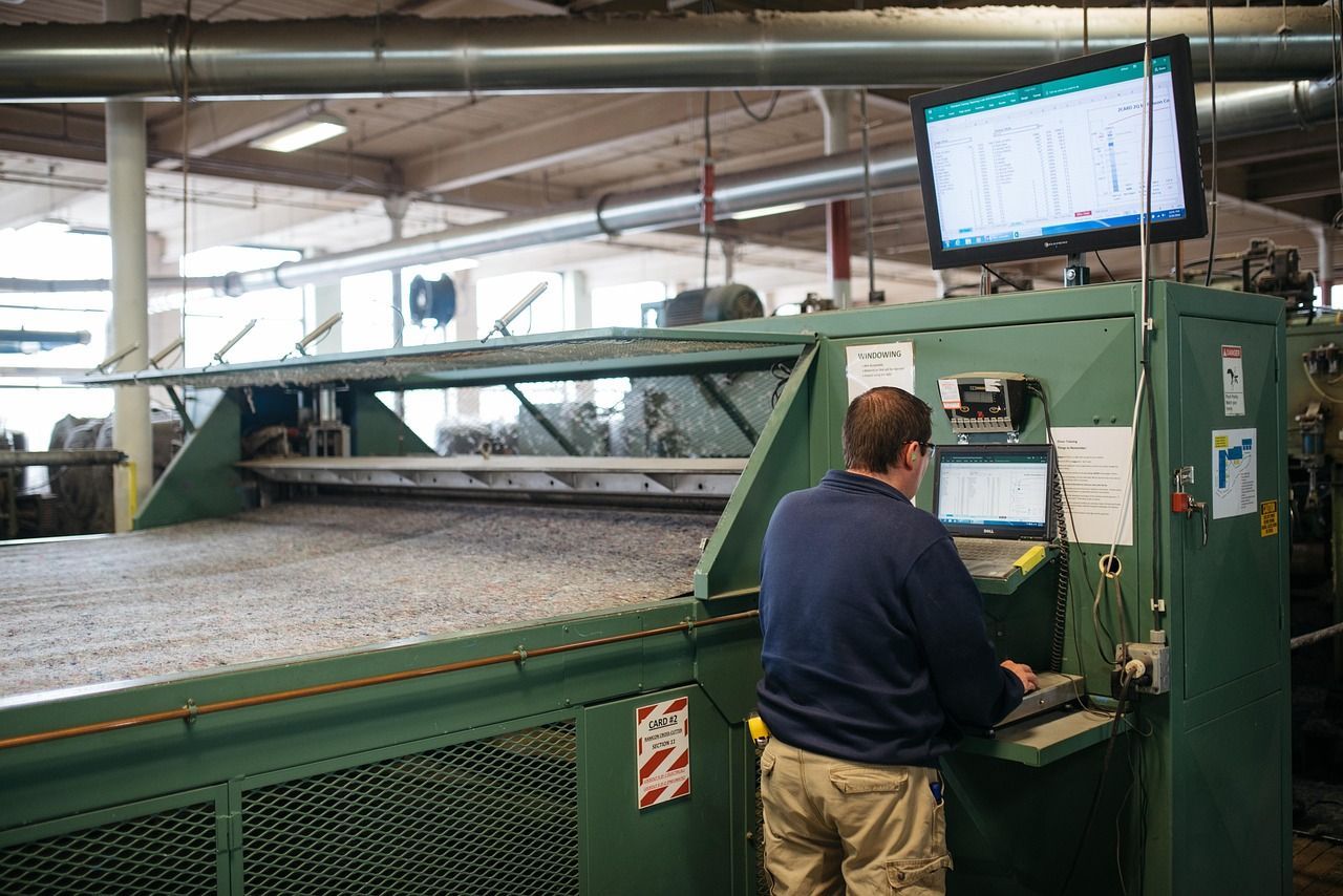 Man at a machine with a computer screen, in a factory setting.