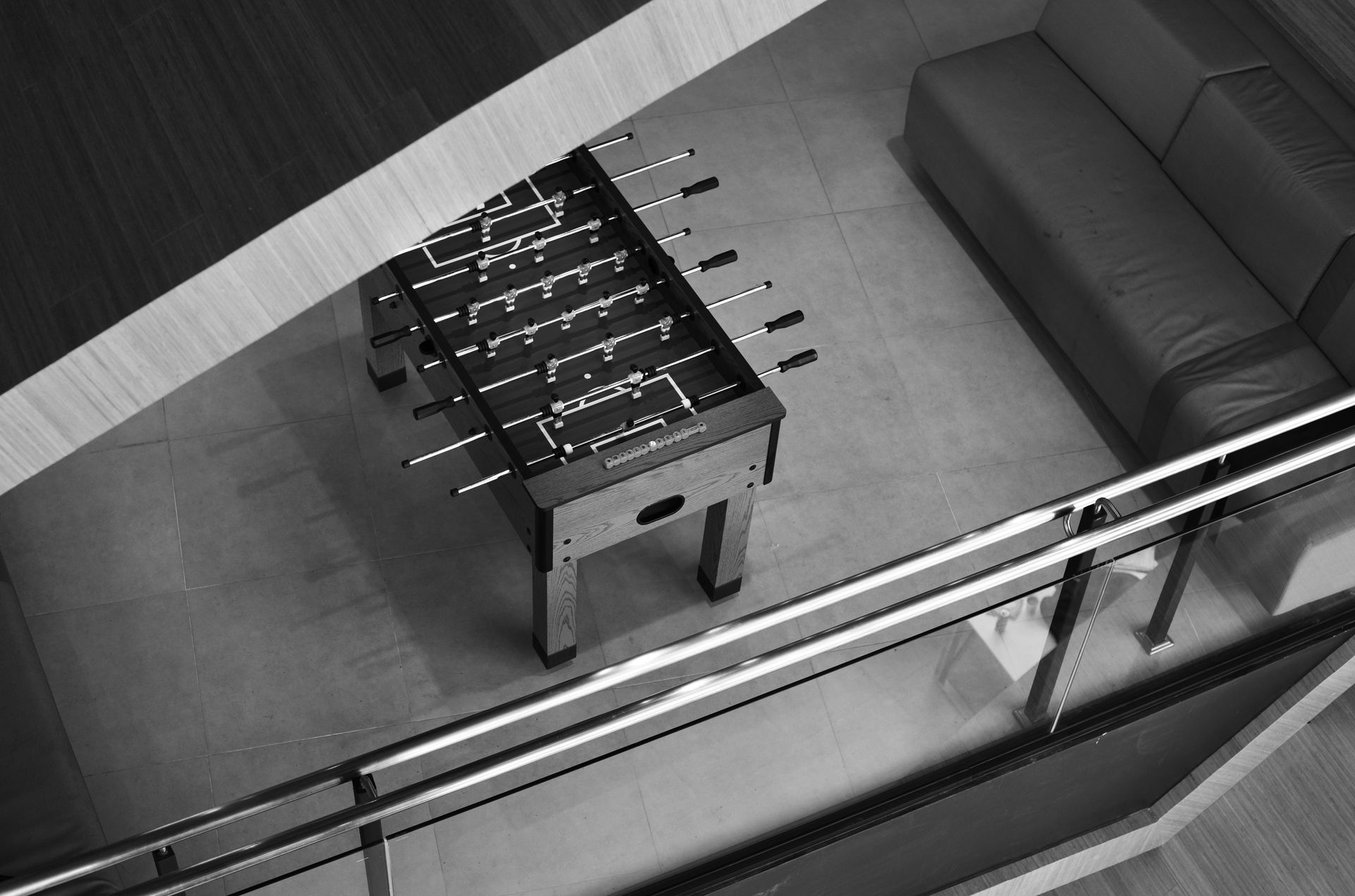 Foosball table, dark wood table, and gray sofa in a modern room, viewed from above.