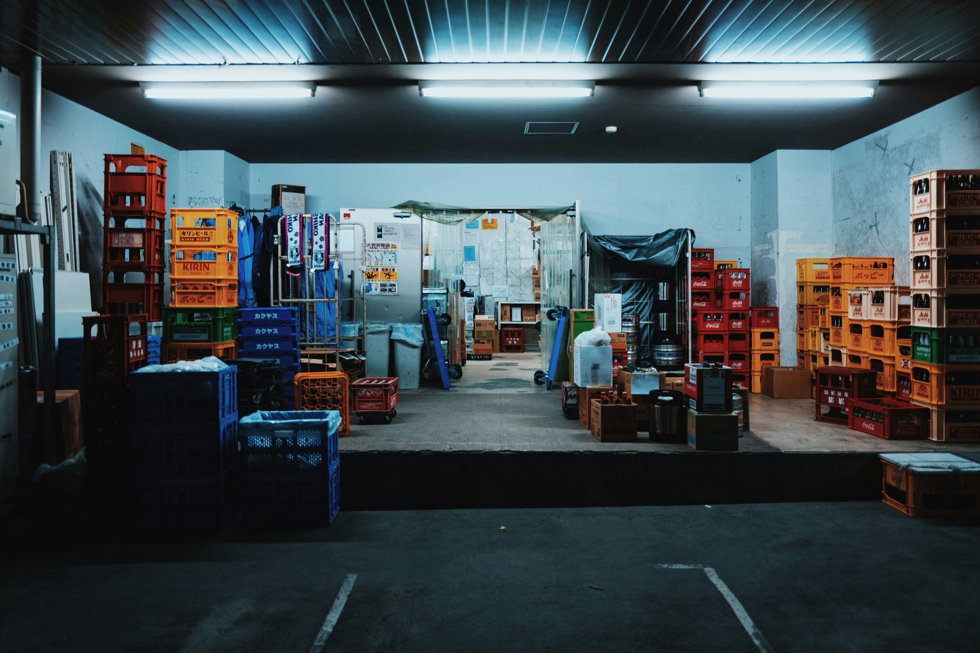 Warehouse interior: Stacks of colorful crates, fluorescent lighting, dimly lit, concrete floor.