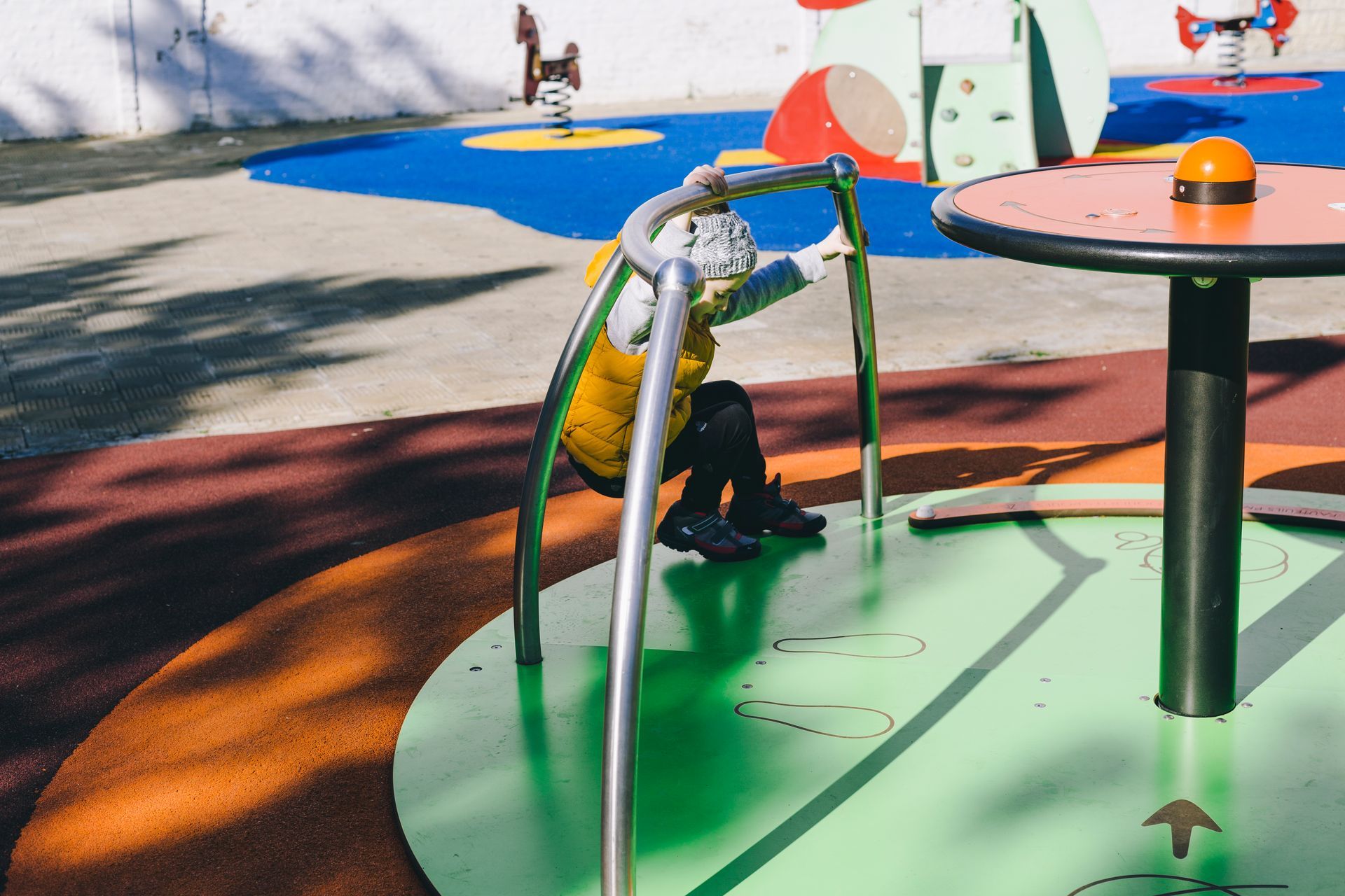 Child in yellow vest playing on a playground merry-go-round.