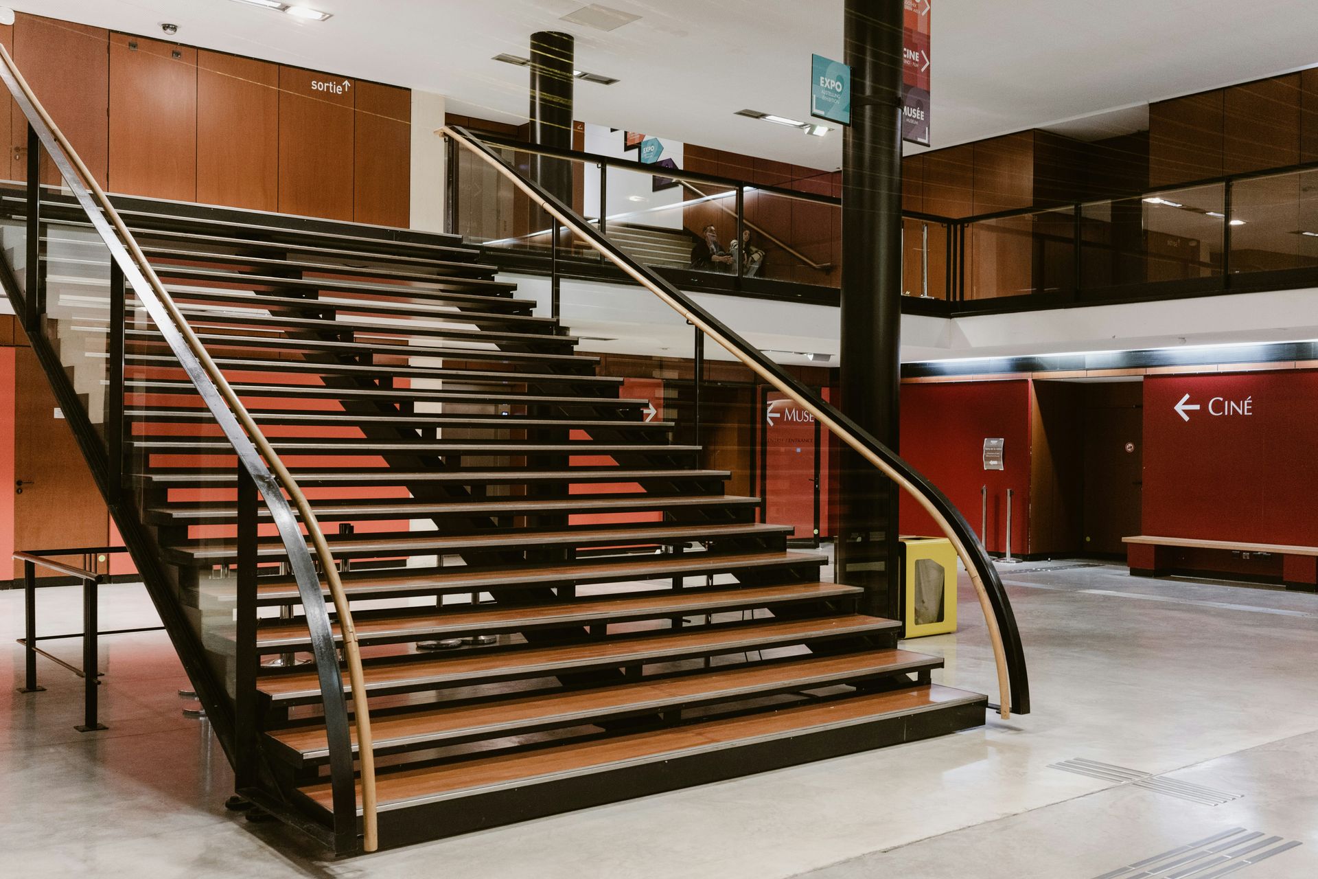A wide staircase with wooden steps and a black metal railing in a public building.