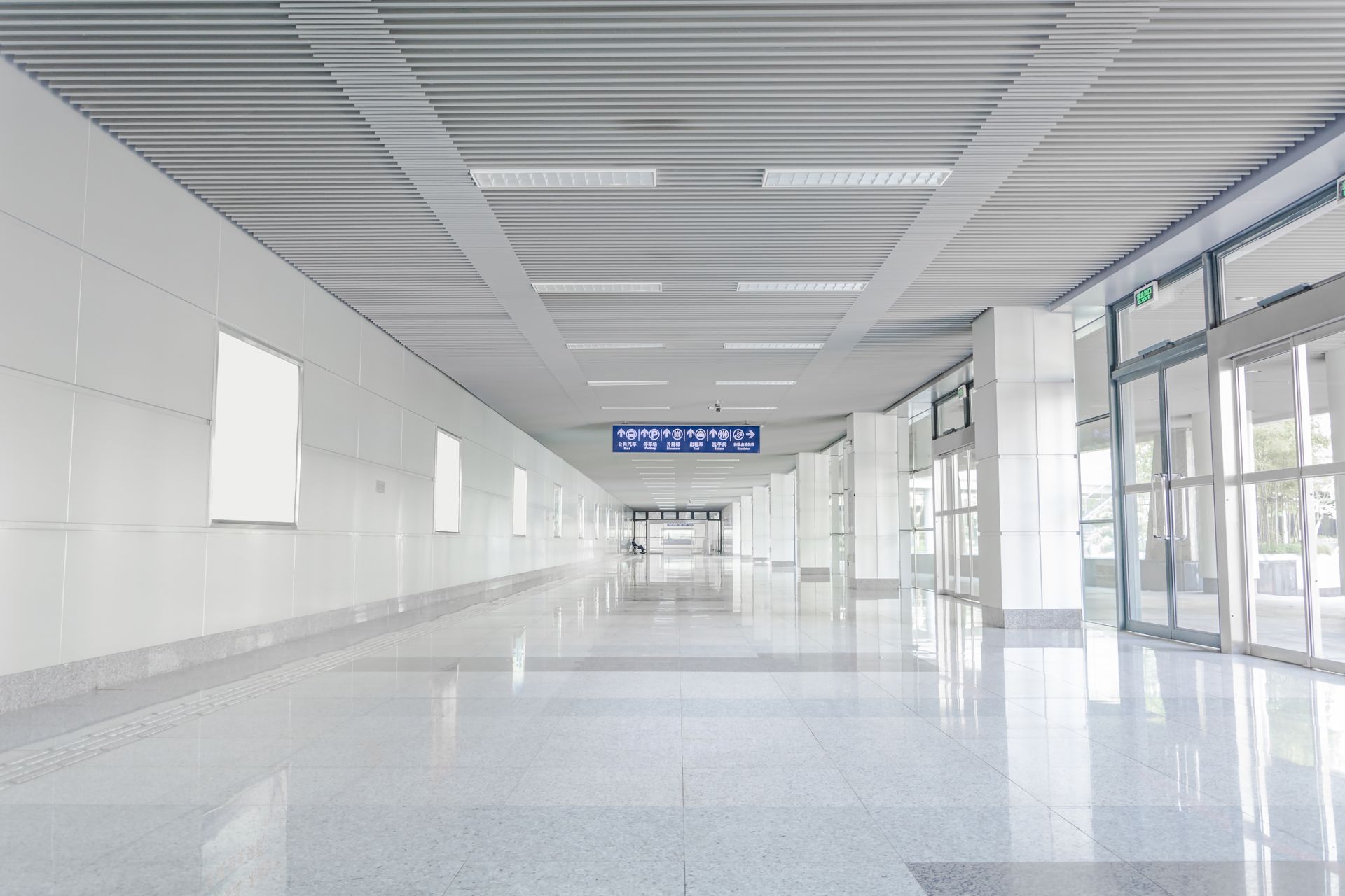 Bright, empty hallway with glossy floor, white walls, and glass doors. Overhead, a metal ceiling and lights.