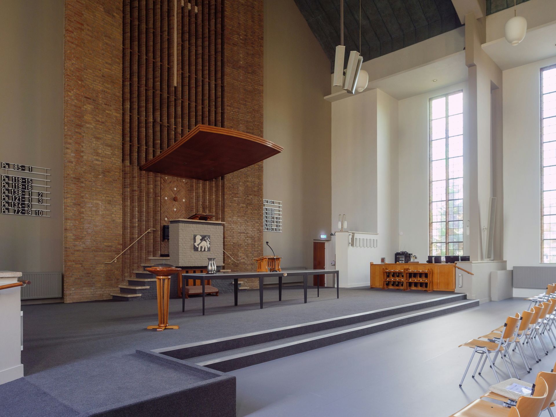 Interior of a modern church with altar, pews, and large windows. Gray and wood tones dominate.
