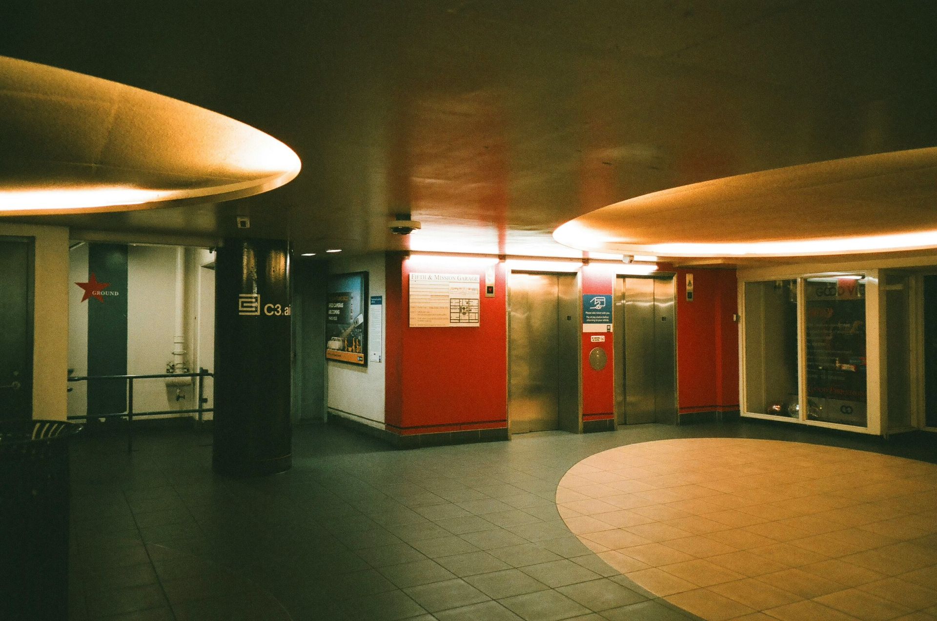 Interior of a building with circular lighting fixtures, elevators, and a red wall.