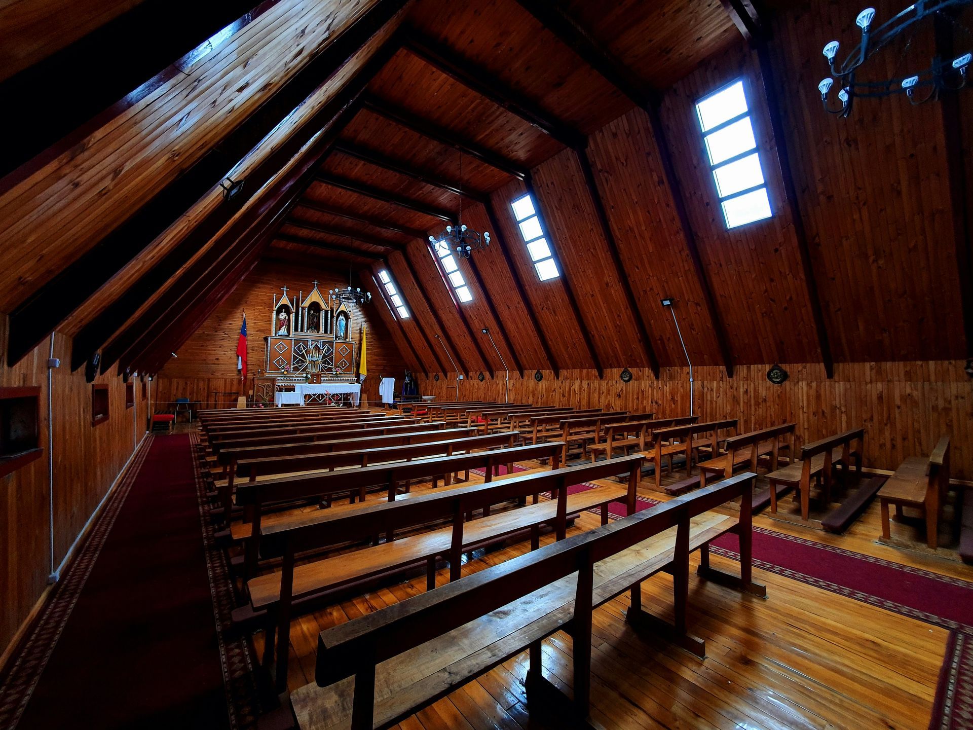 Interior of a wooden church with rows of pews facing an altar. Sunlight streams through the windows.