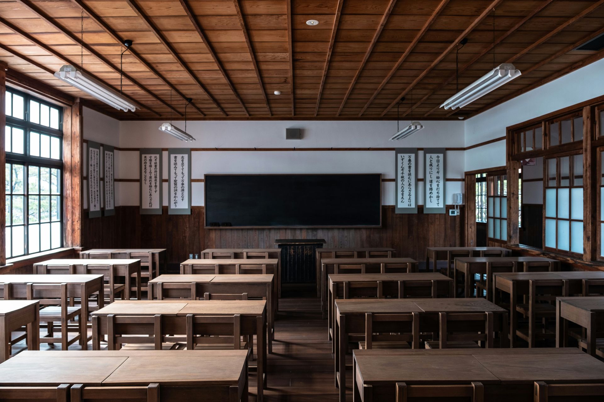 Empty vintage classroom with wooden desks, chalkboard, and windows.