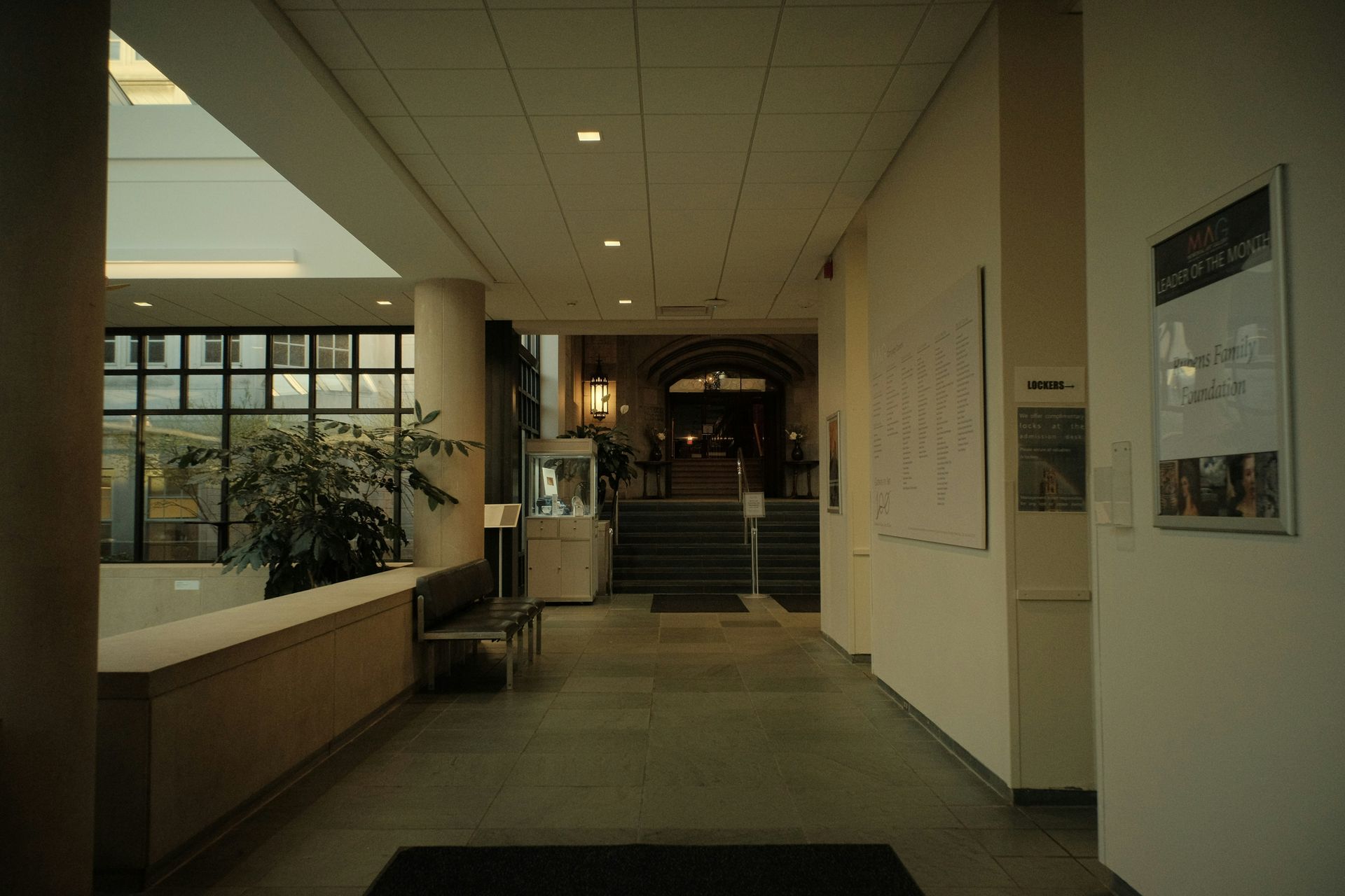 Hallway in building with windows, stairs, and plants. Neutral color scheme, natural light.