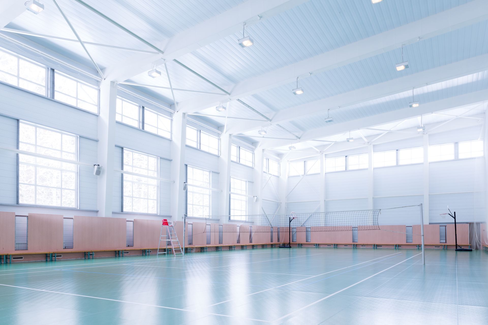 Bright, empty gymnasium with windows, light-blue floor, and safety barriers.