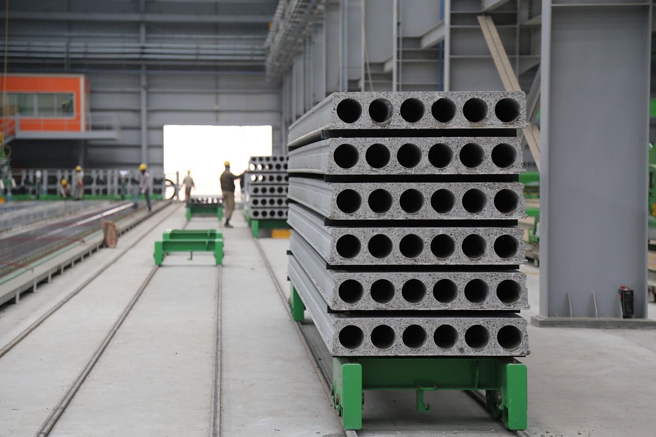 Stack of precast concrete slabs with circular holes on a rail in a factory, workers visible in the background.