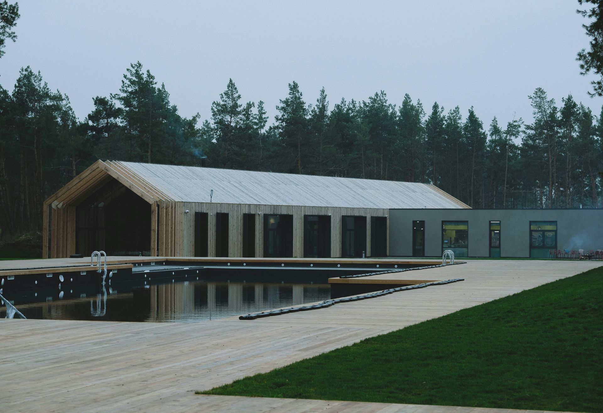 A modern wooden building with a pool, set in a forest.
