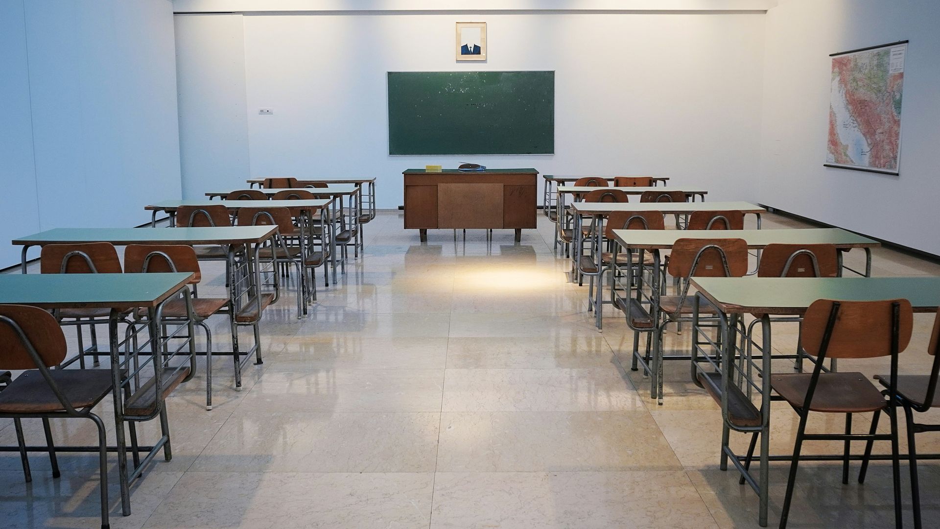 Empty classroom with rows of desks, windows, and natural light streaming in.