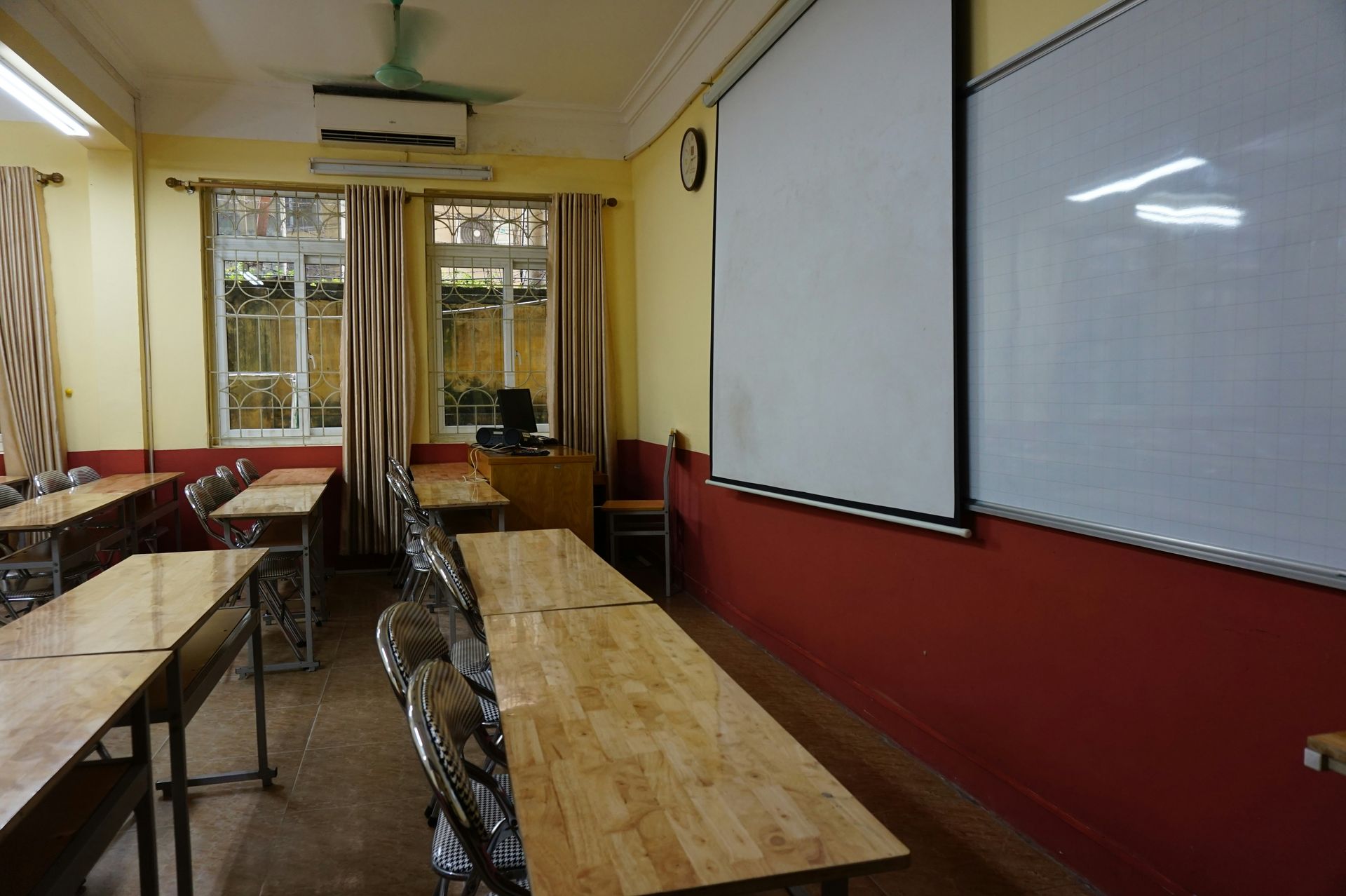 Empty classroom with wooden desks, whiteboards, and a window.