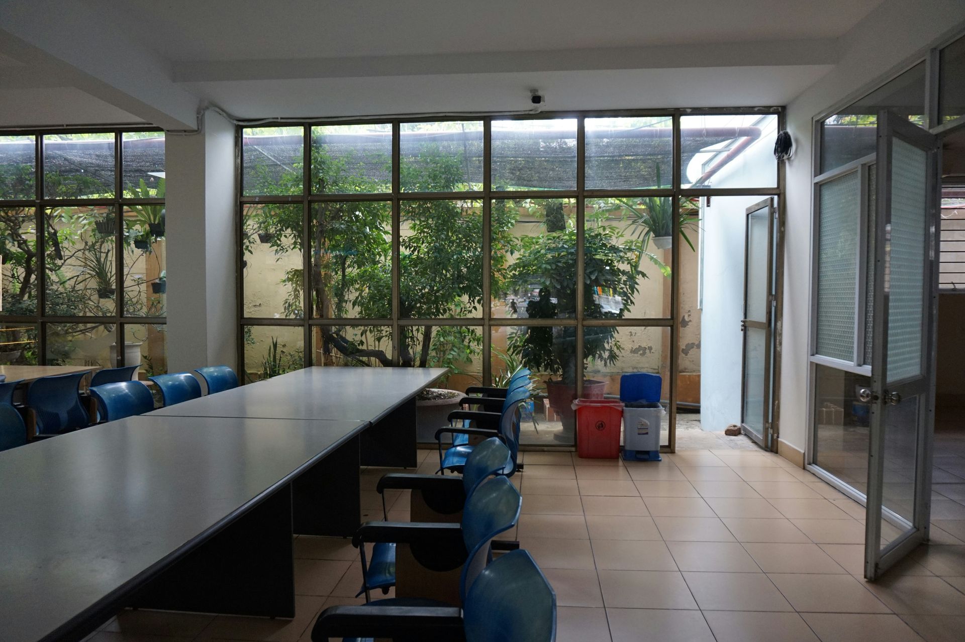 Meeting room with long table, blue chairs, large windows overlooking greenery. Open glass door.