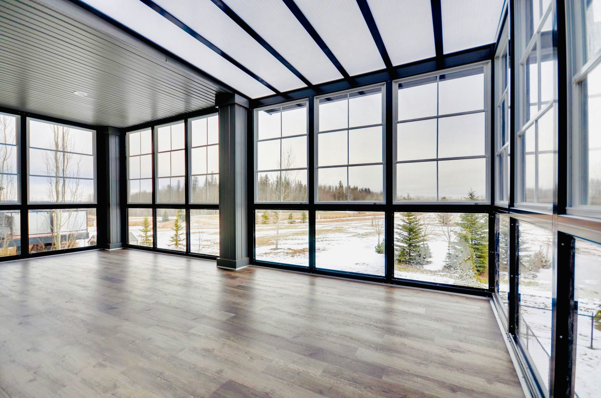 Sunroom with large windows, black frames, and a view of a snowy landscape.