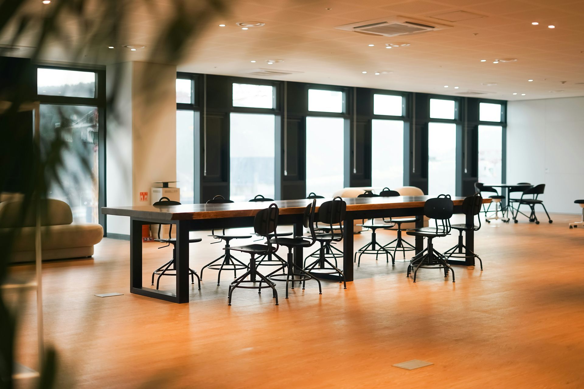 A large open office space with a long table and chairs near large windows.