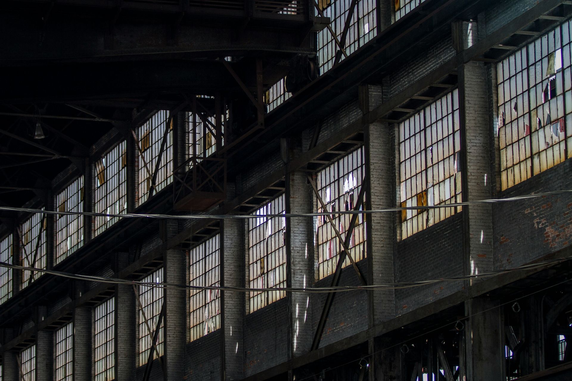 Interior of an old industrial building, with rows of windows casting light onto rusted metal beams.