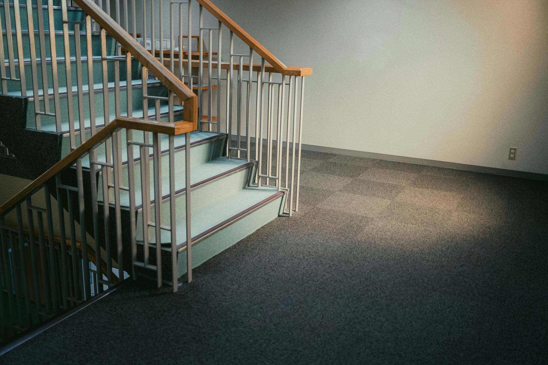 Staircase with white metal railings and light green steps, leading up with dark carpet floor.