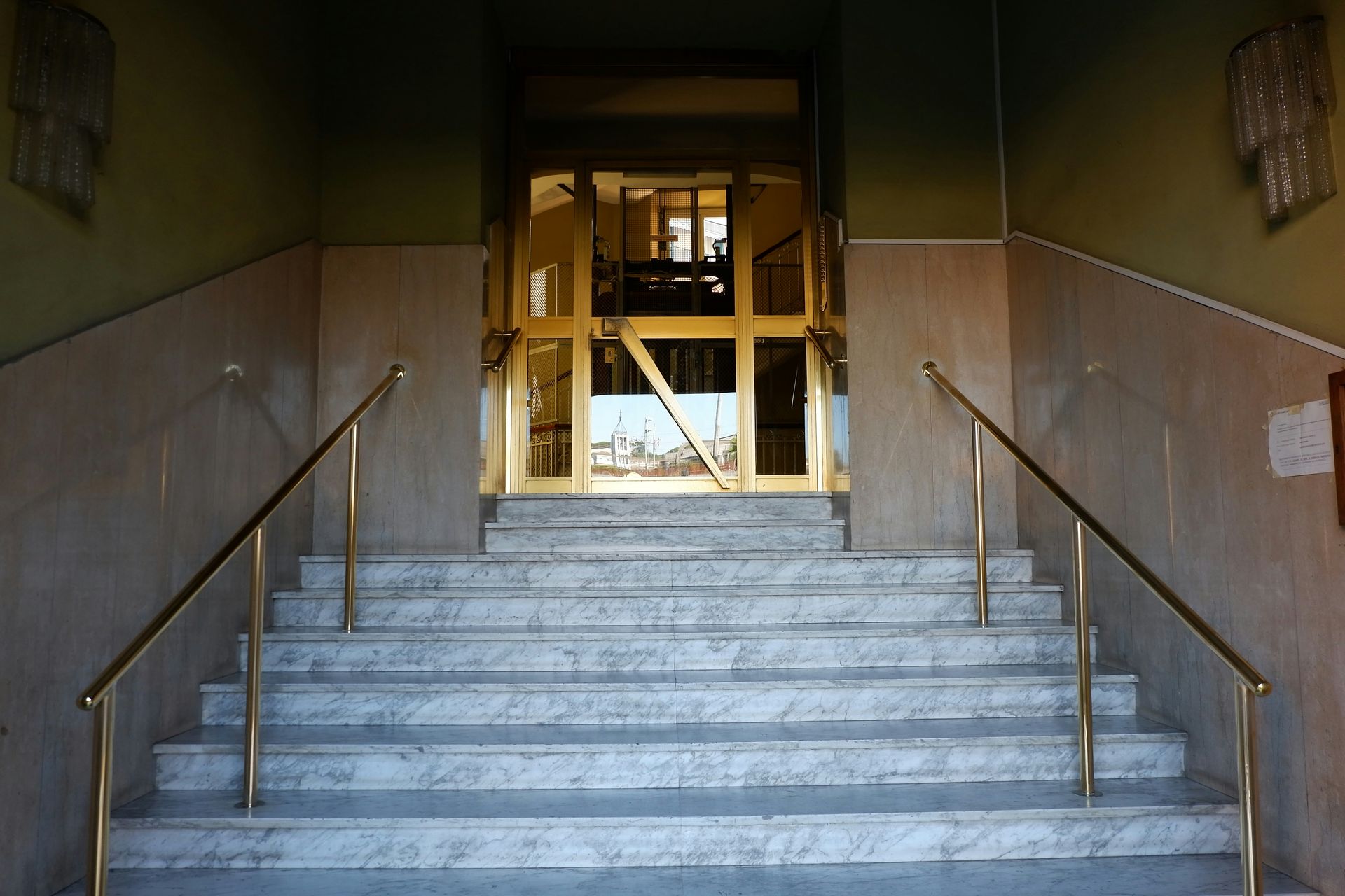 Marble steps leading to a gold door; brass handrails on either side.