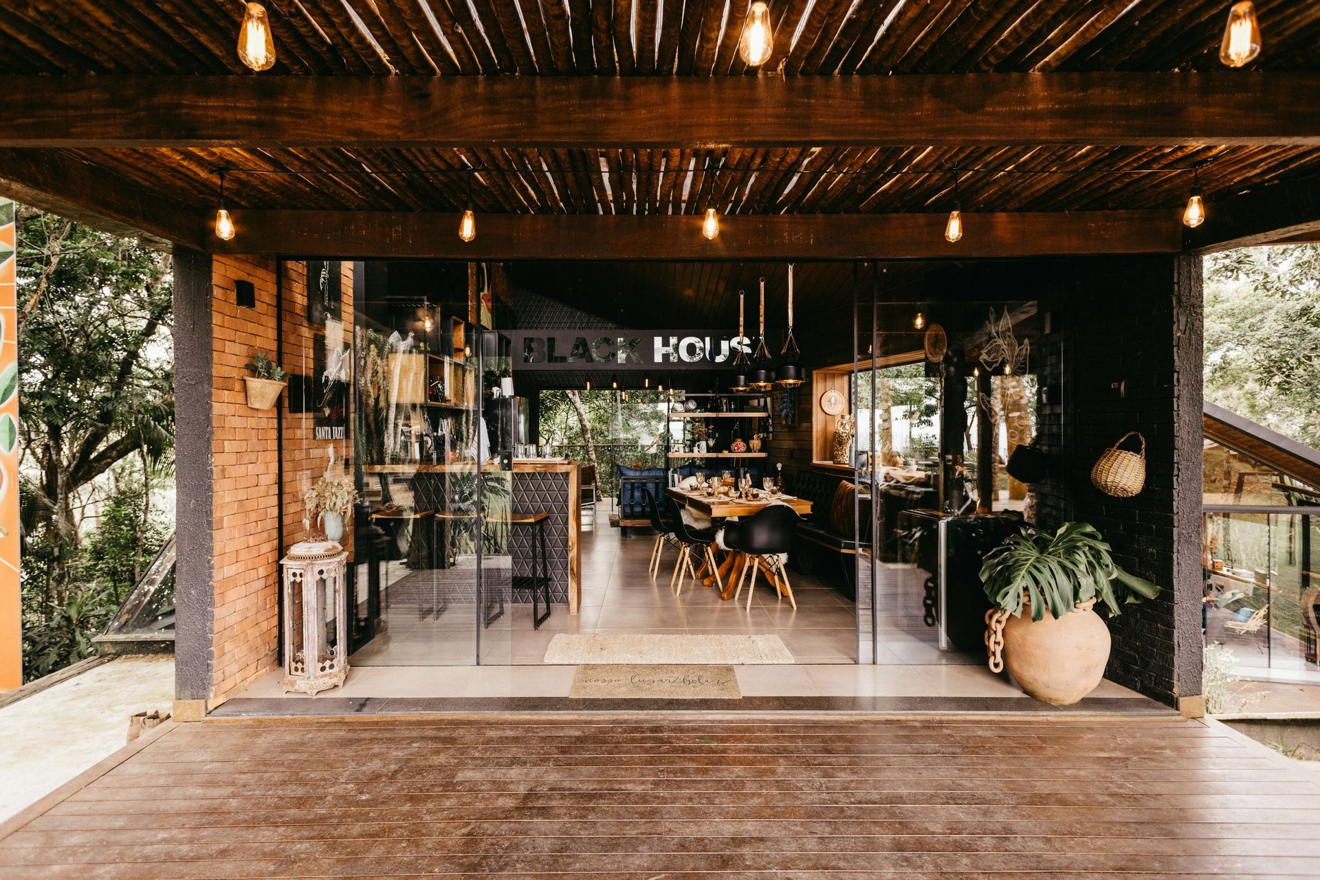 Exterior view of a restaurant with glass doors, wooden deck, and string lights.