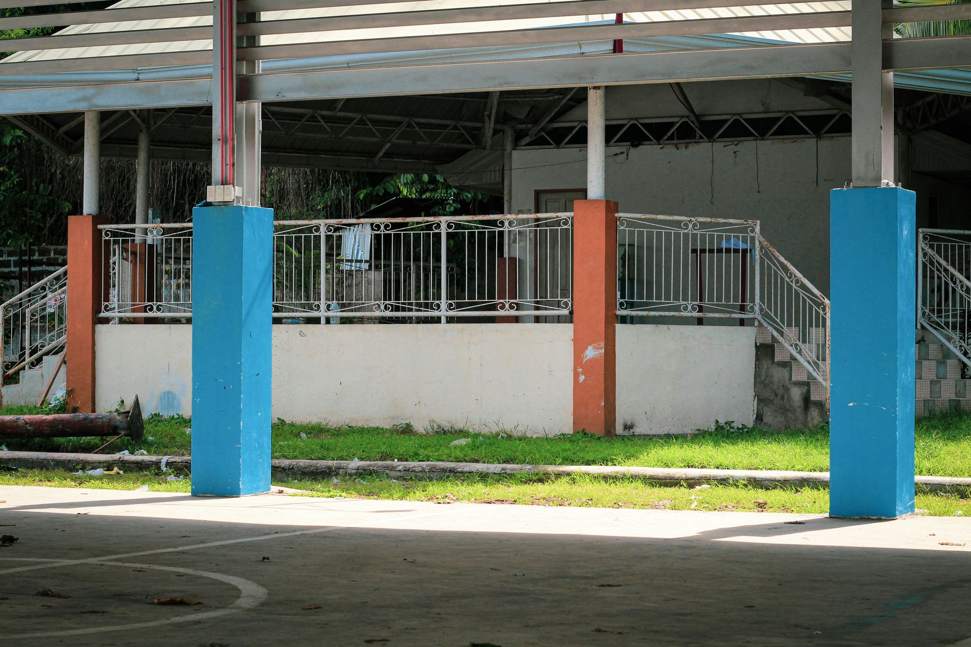 Two blue support pillars in the foreground. A white building with a railing and stairs is in the background.