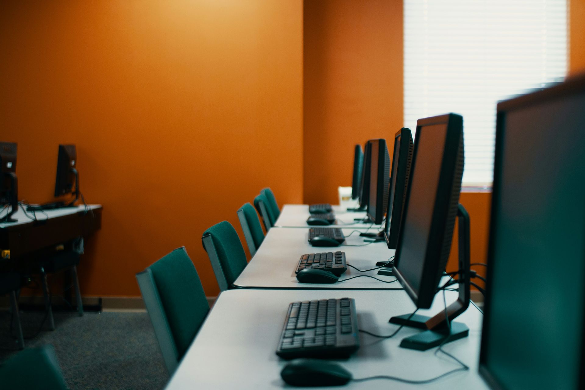 Computer lab with orange walls and rows of computers on white desks.