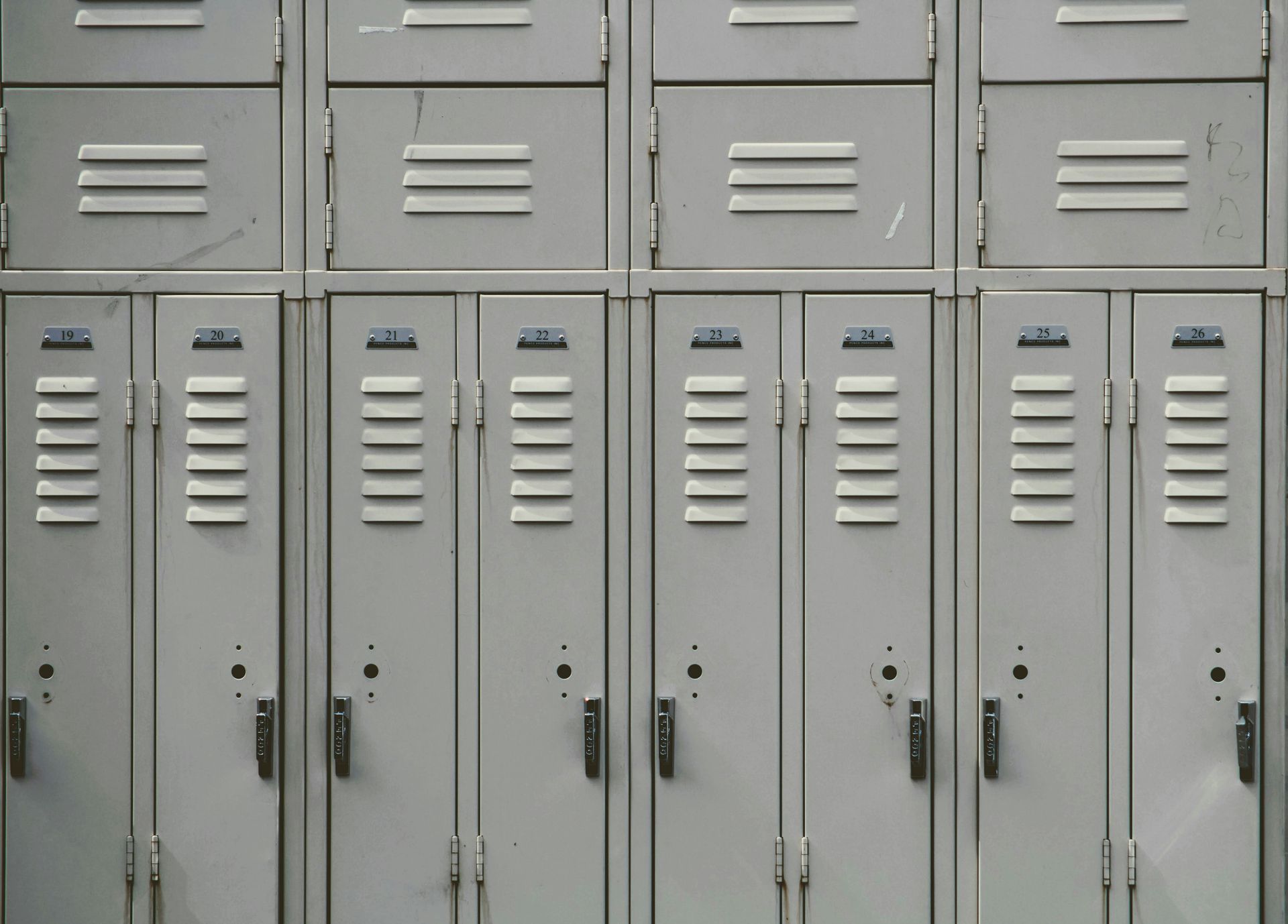Rows of gray school lockers in a hallway, with ventilation slots and combination locks.