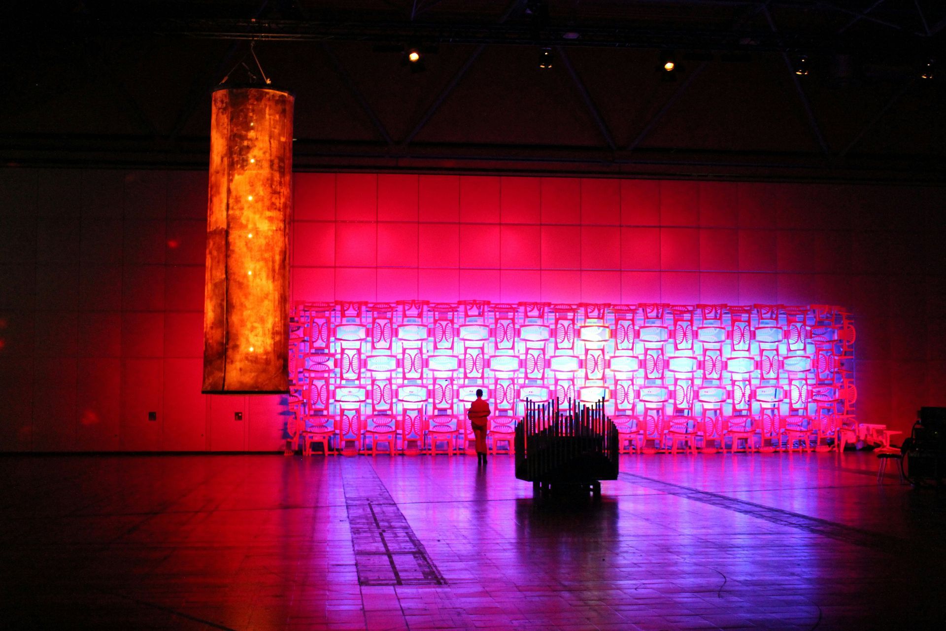 An art installation of a large glowing cylinder and a red-lit wall with intricate patterns. A person stands in front.