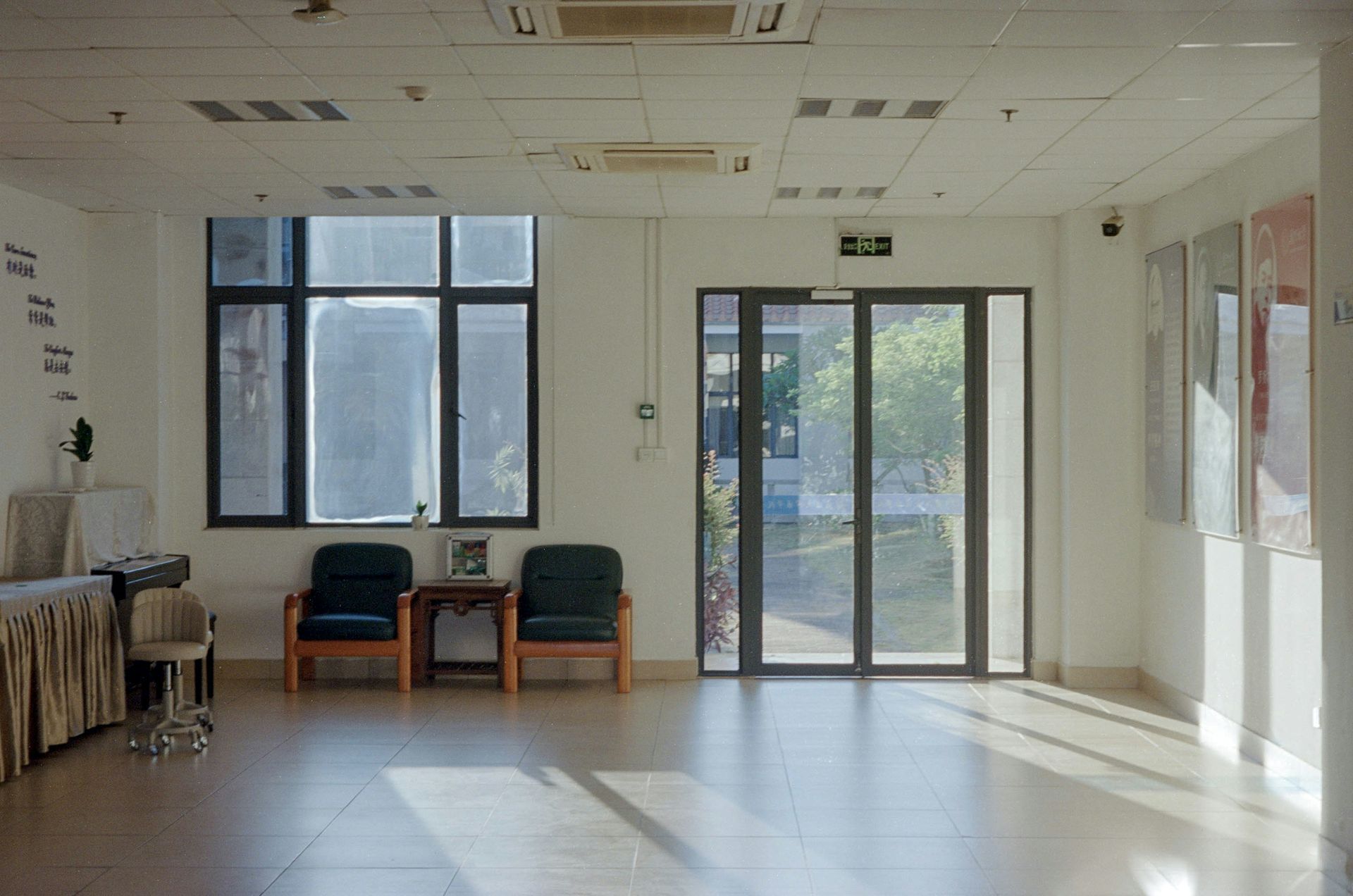 Long empty corridor with a red ceiling and glass storefronts reflecting outdoor trees.