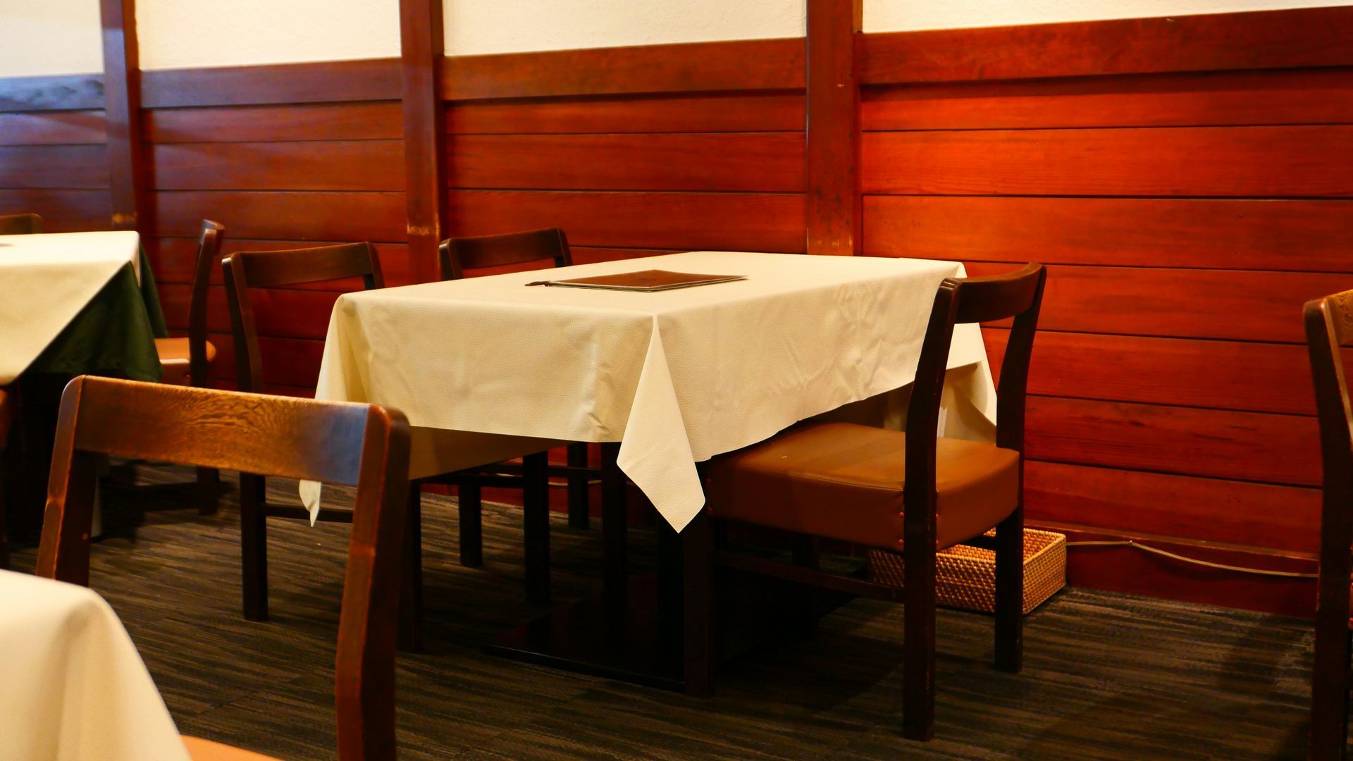 Dining room with wooden walls and tables set with white tablecloths, brown chairs.