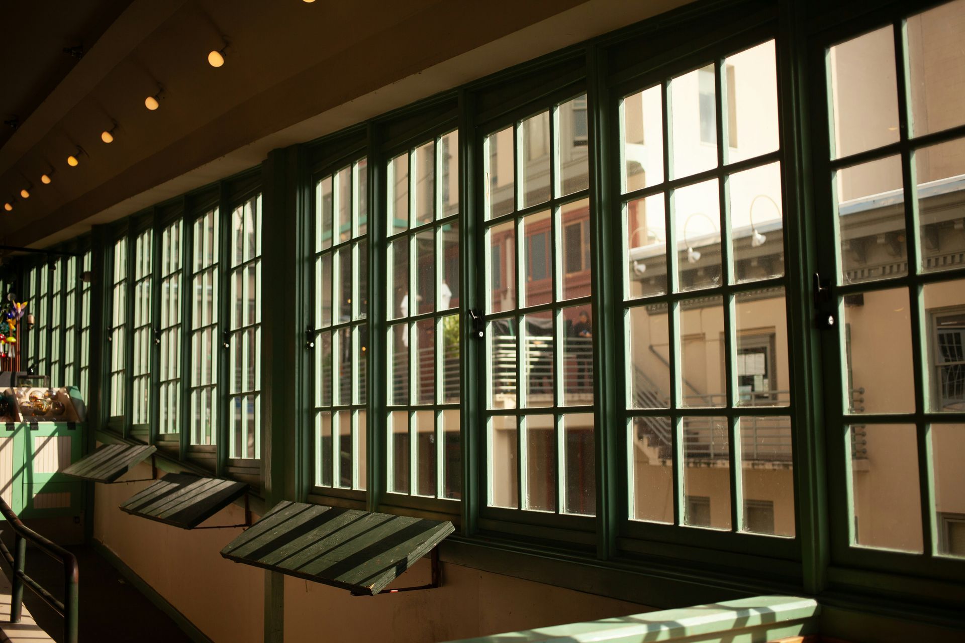 Row of green-framed windows overlooking buildings, with sunlight streaming through.