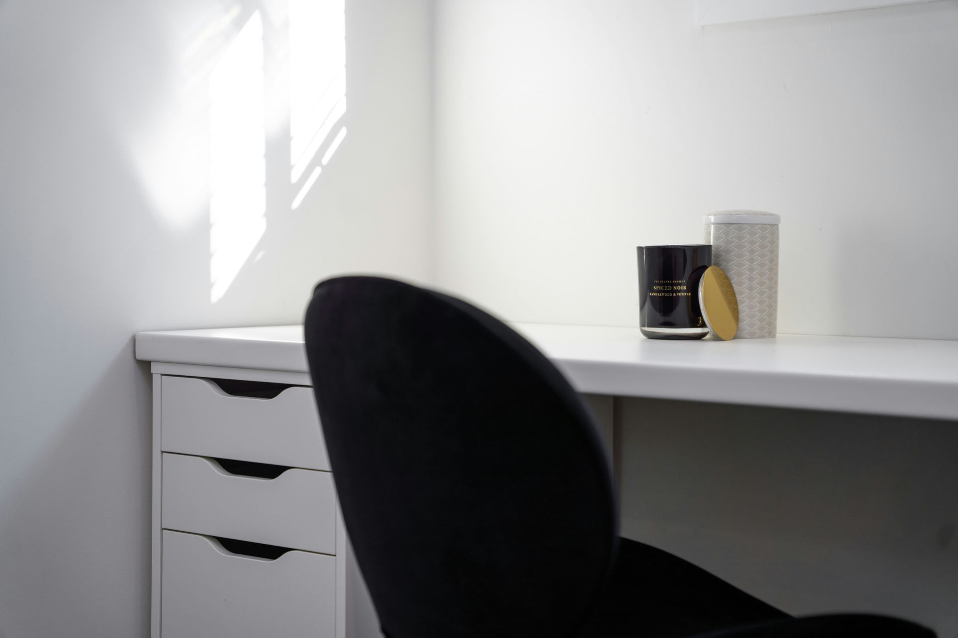 Desk in a white room with a black chair, featuring three decorative items on the tabletop.