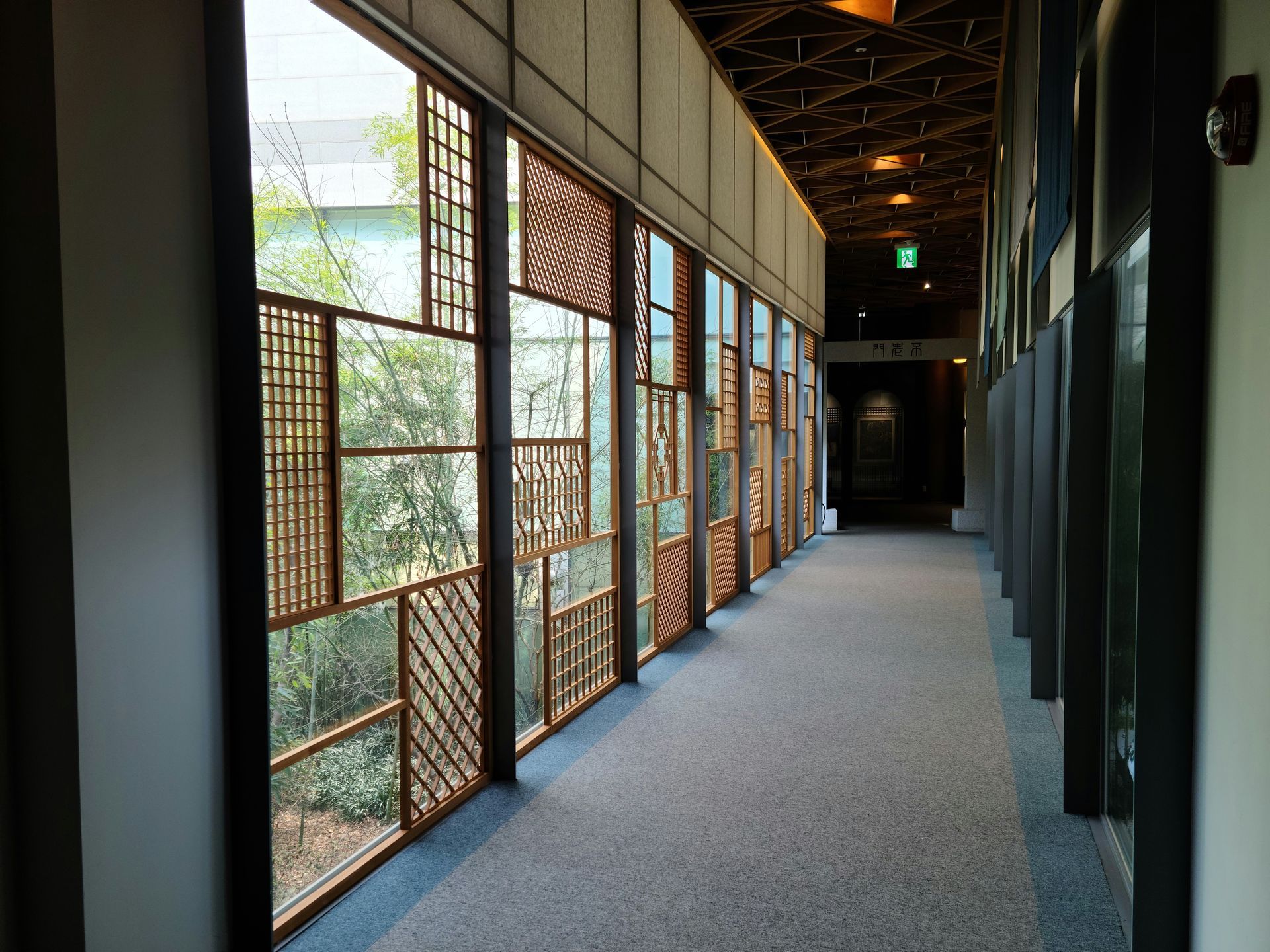Long hallway with patterned windows to the left, leading to a dark doorway at the end.