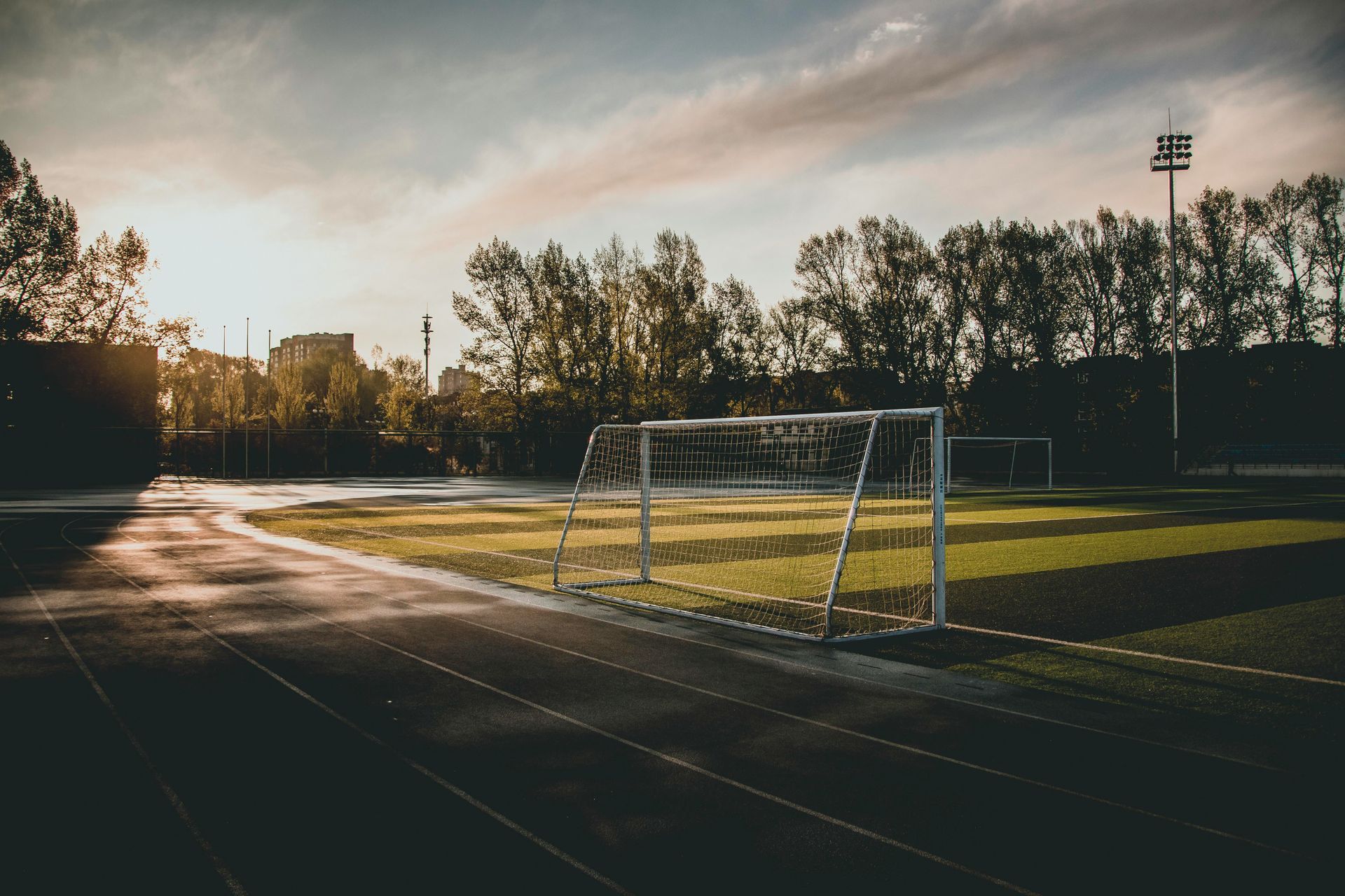 Soccer field at sunset with goal in the foreground and trees in the background.