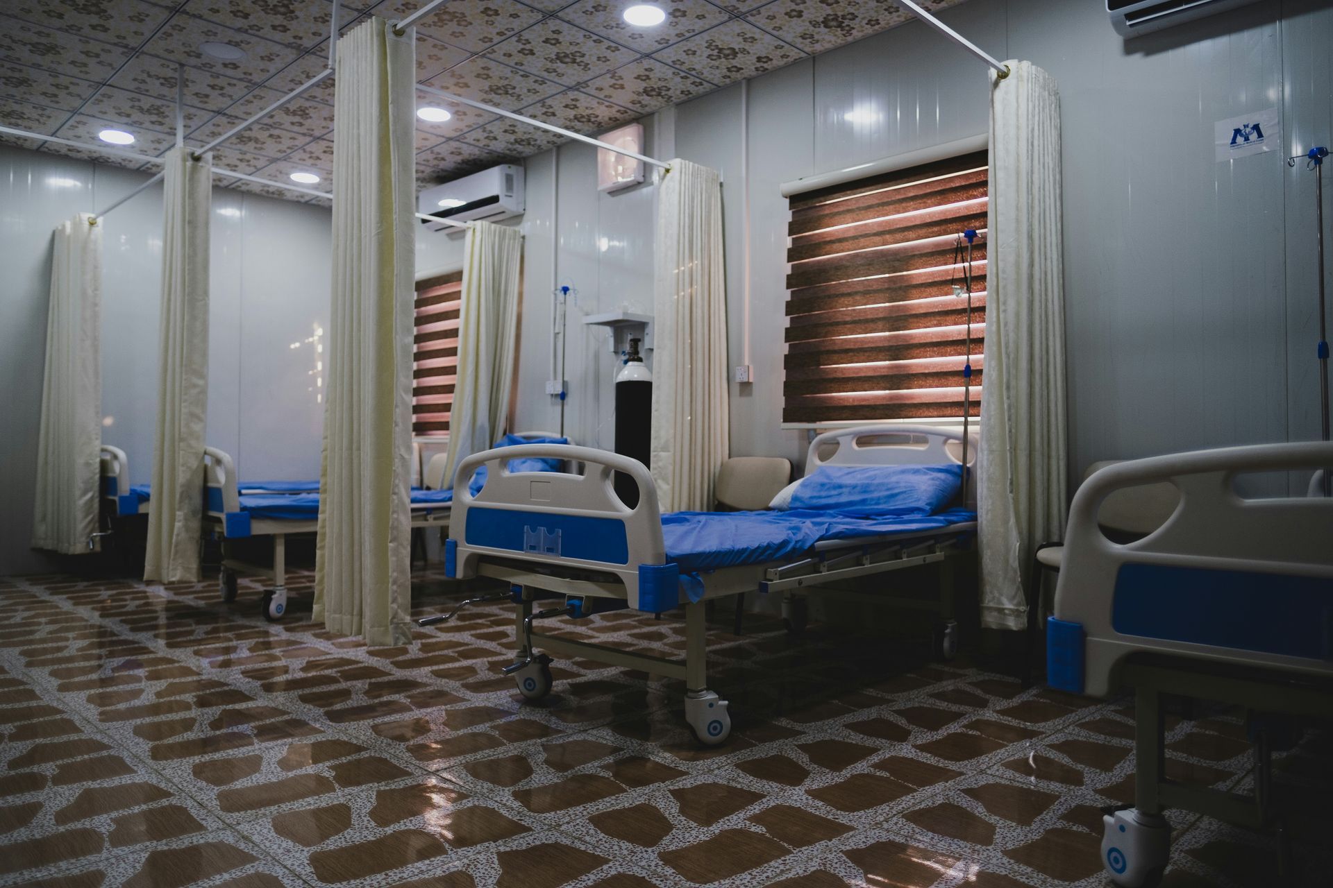 Hospital room with several beds, curtains, and a tiled floor.