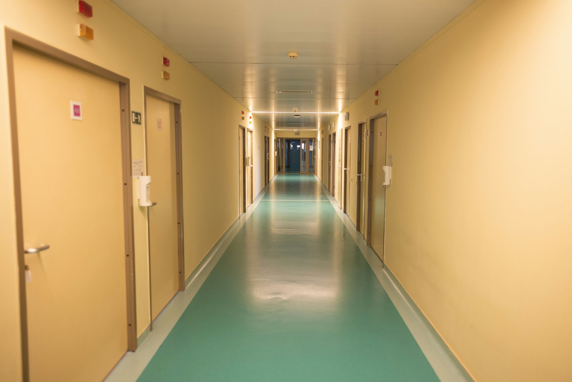 Long hallway with doors on both sides, teal floor, and yellow walls.