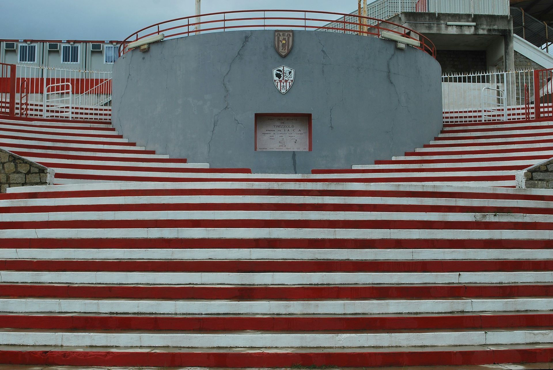 Red and white stadium steps leading up to a gray concrete structure with a crest.