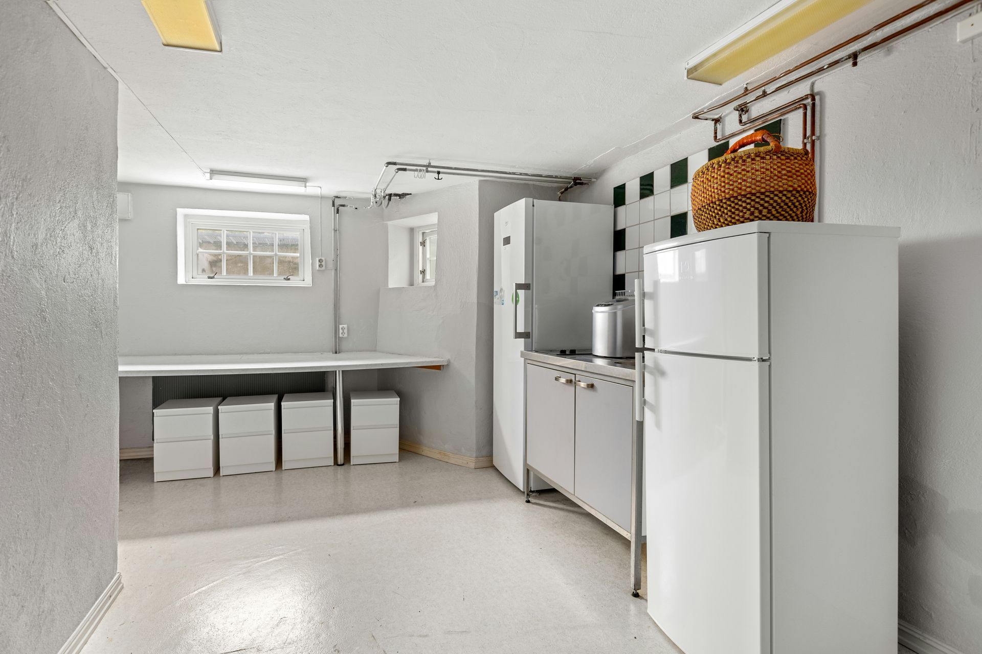 Basement with white appliances, a long counter, and storage. A wicker basket sits atop cabinets.