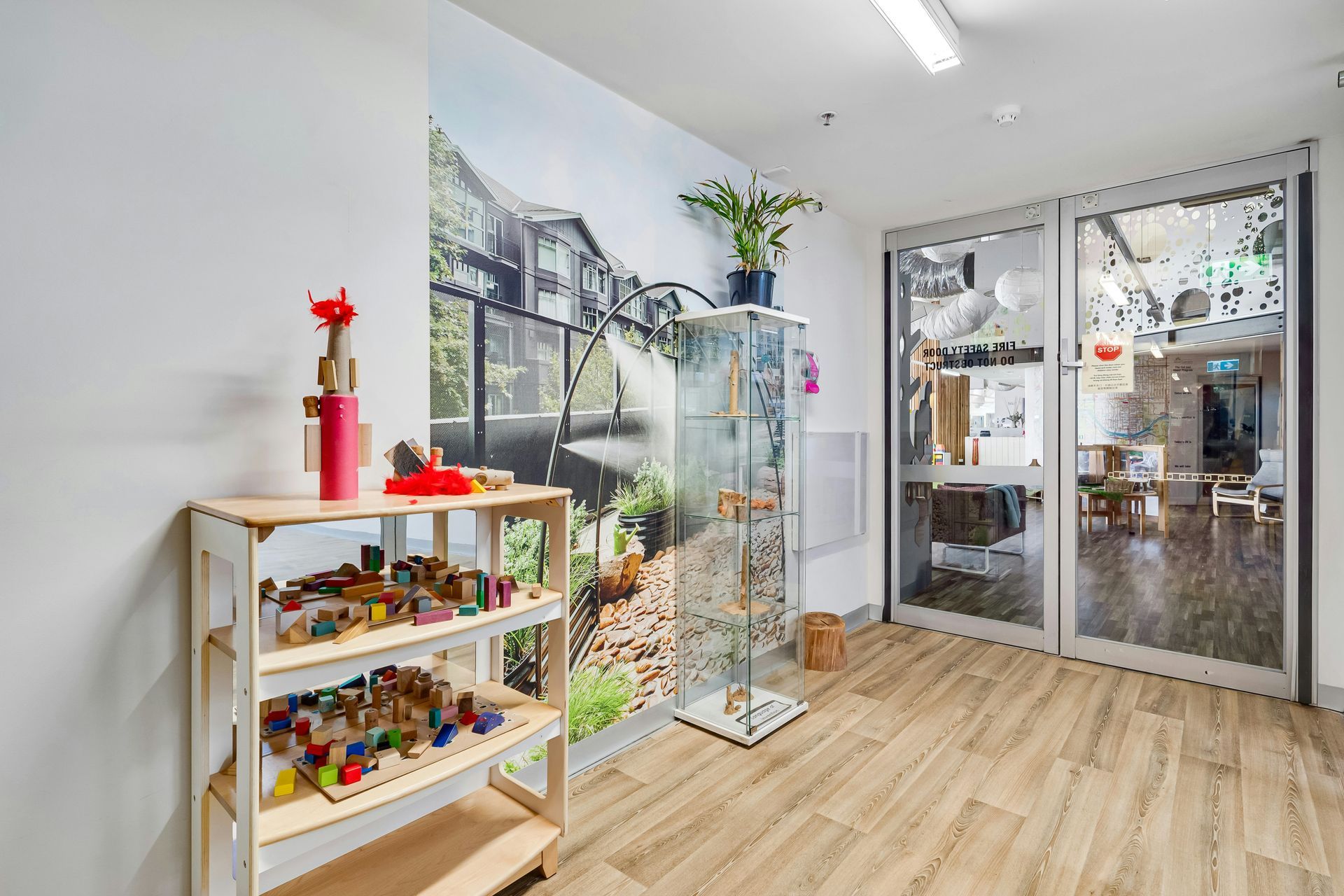 Hallway with wooden shelves holding toys, a glass display case, and a door to a brightly lit room.