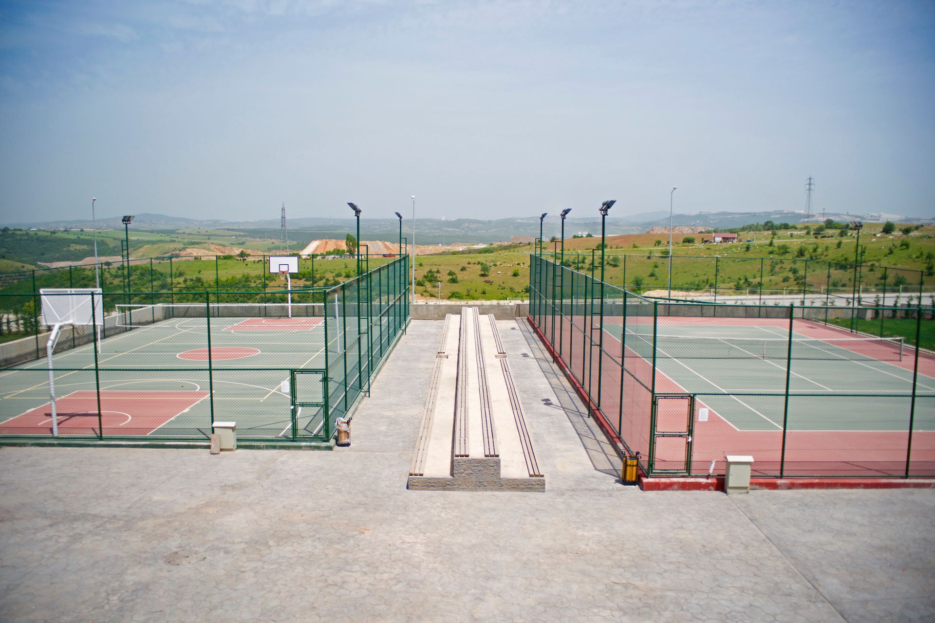 Outdoor basketball and tennis courts side by side, separated by a walkway, with a scenic landscape in the background.