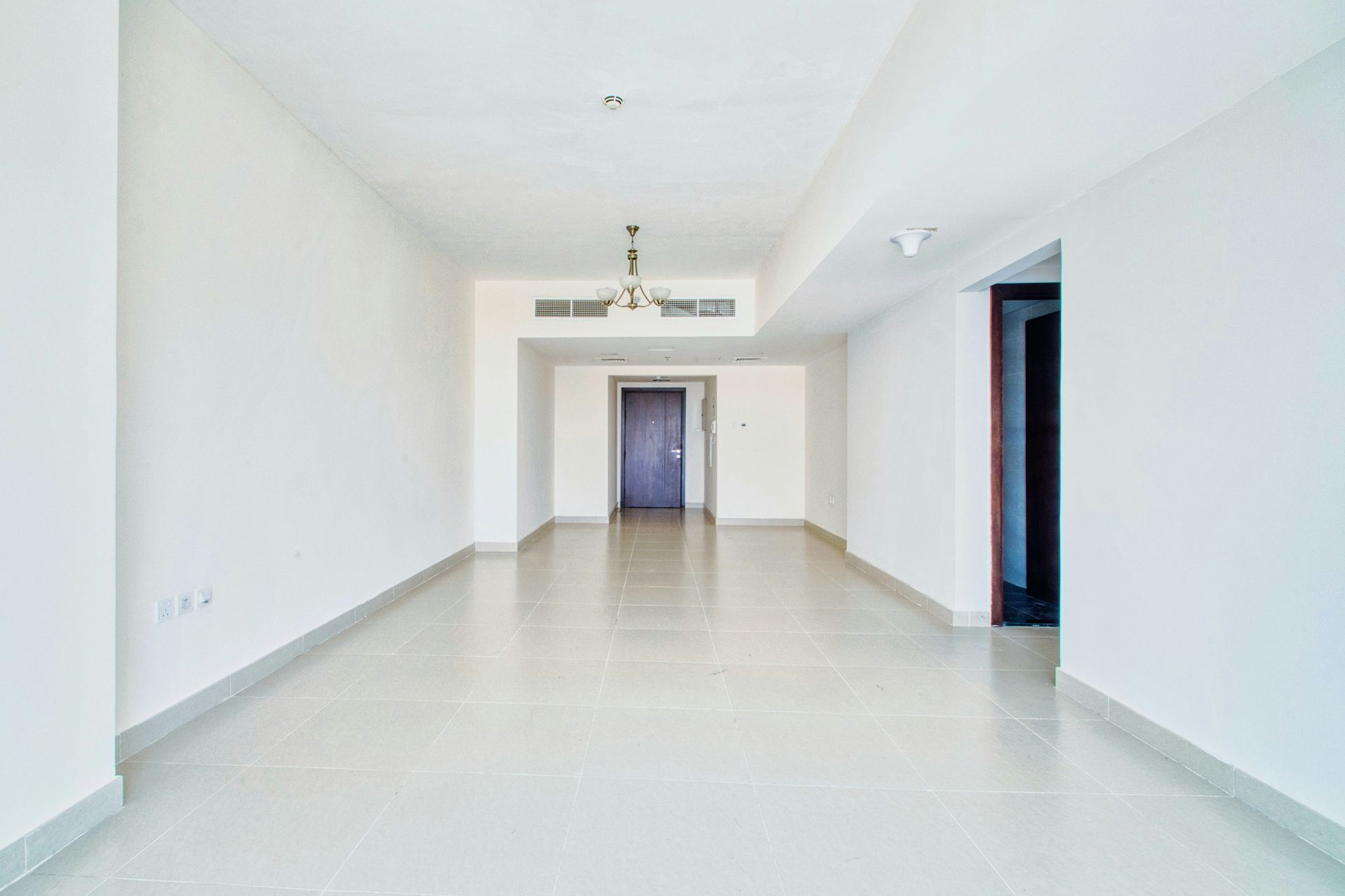 Empty, bright room with white walls and tiled floor, leading to a closed door.