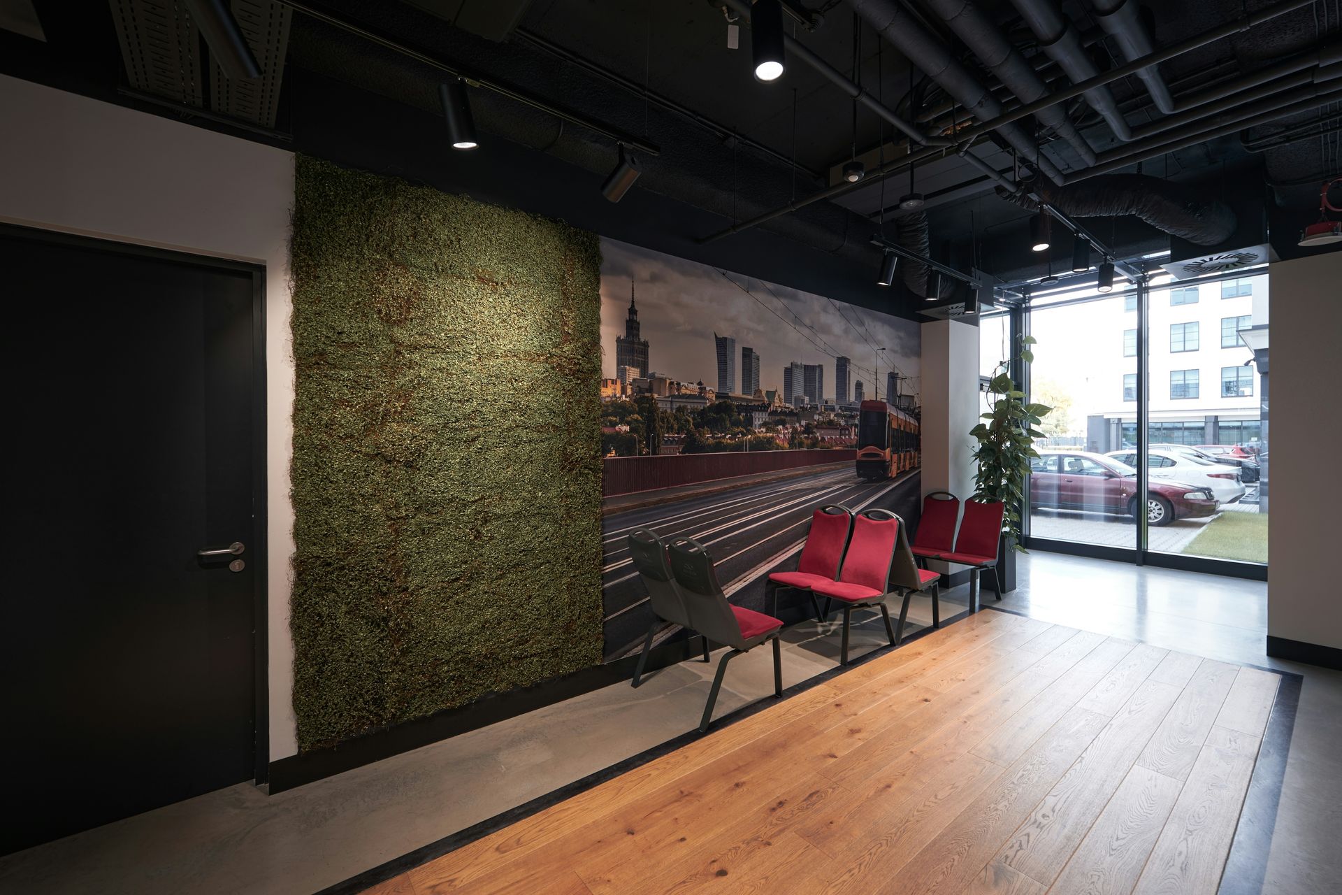 Lobby with a green wall, city mural, red chairs, and glass window overlooking a parking area.
