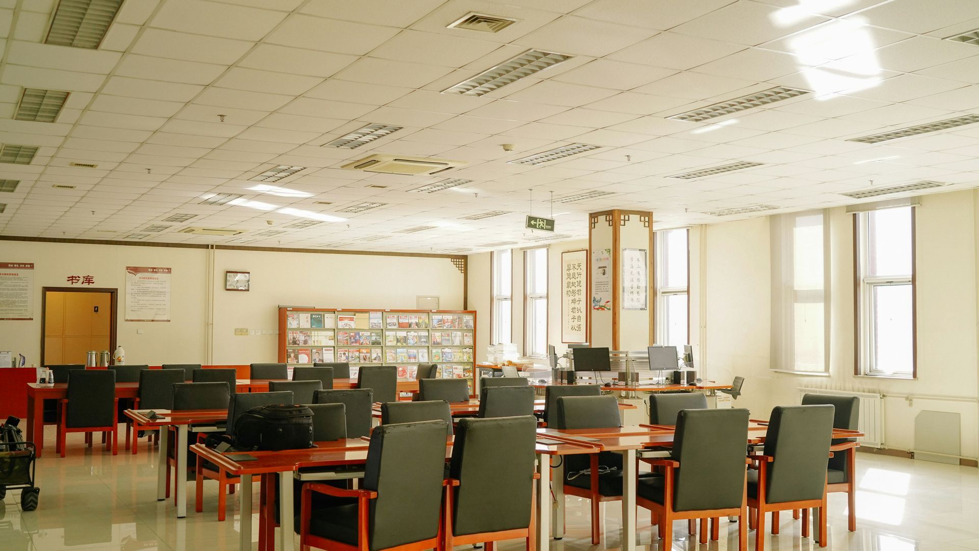 An interior shot of a library with tables, chairs, computers, and windows.