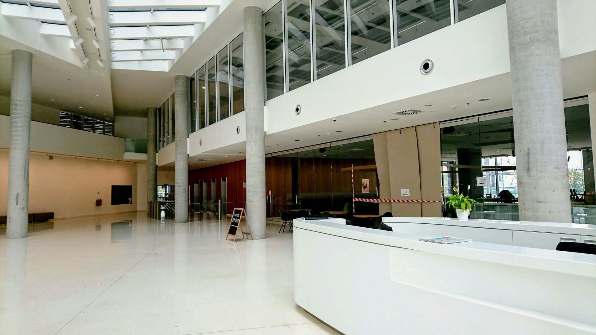 Large, bright, open lobby with white floor and columns, reception desk, and glass windows.
